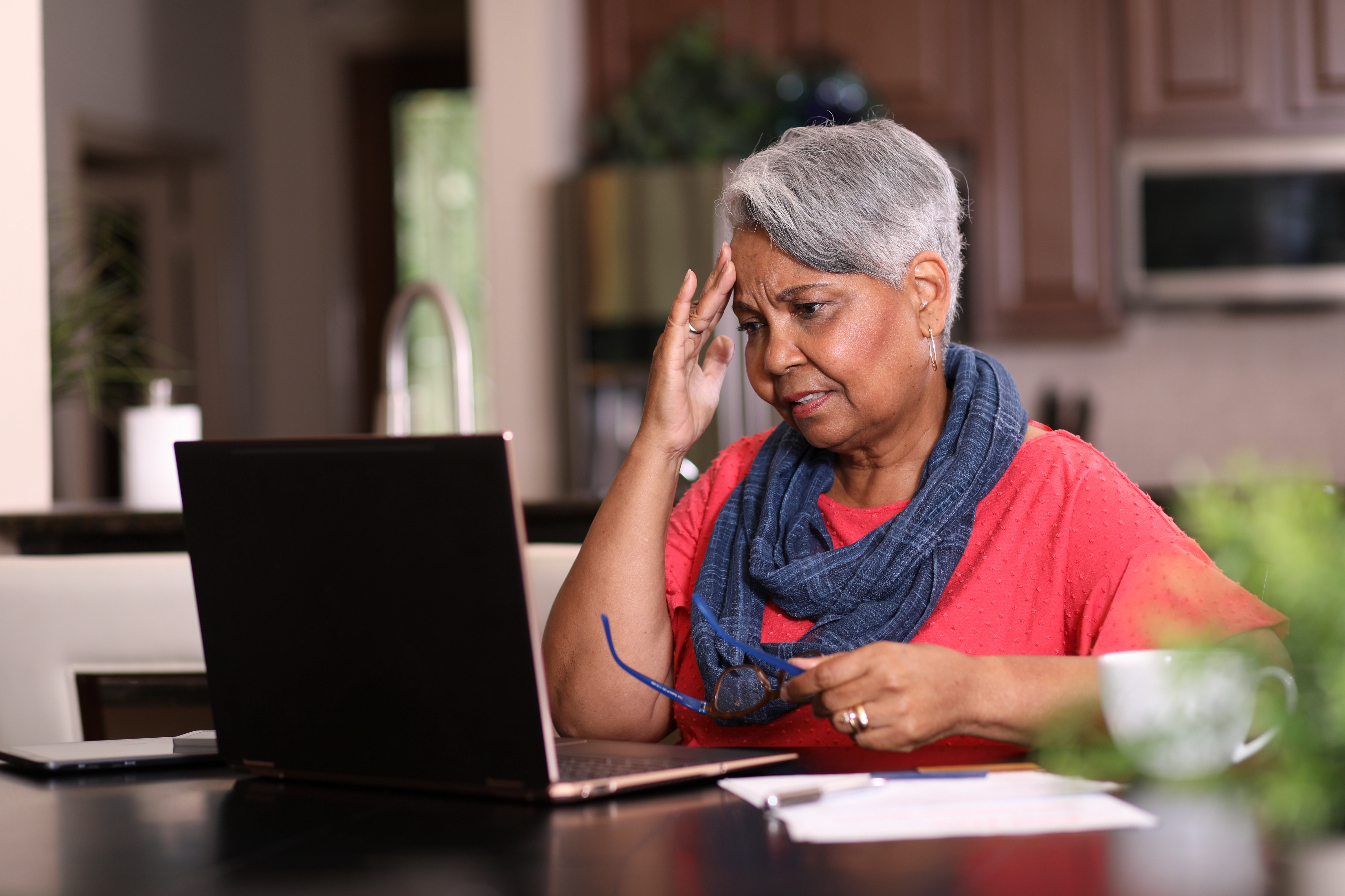 Woman with short gray hair looks concerned while using a laptop, holding her glasses