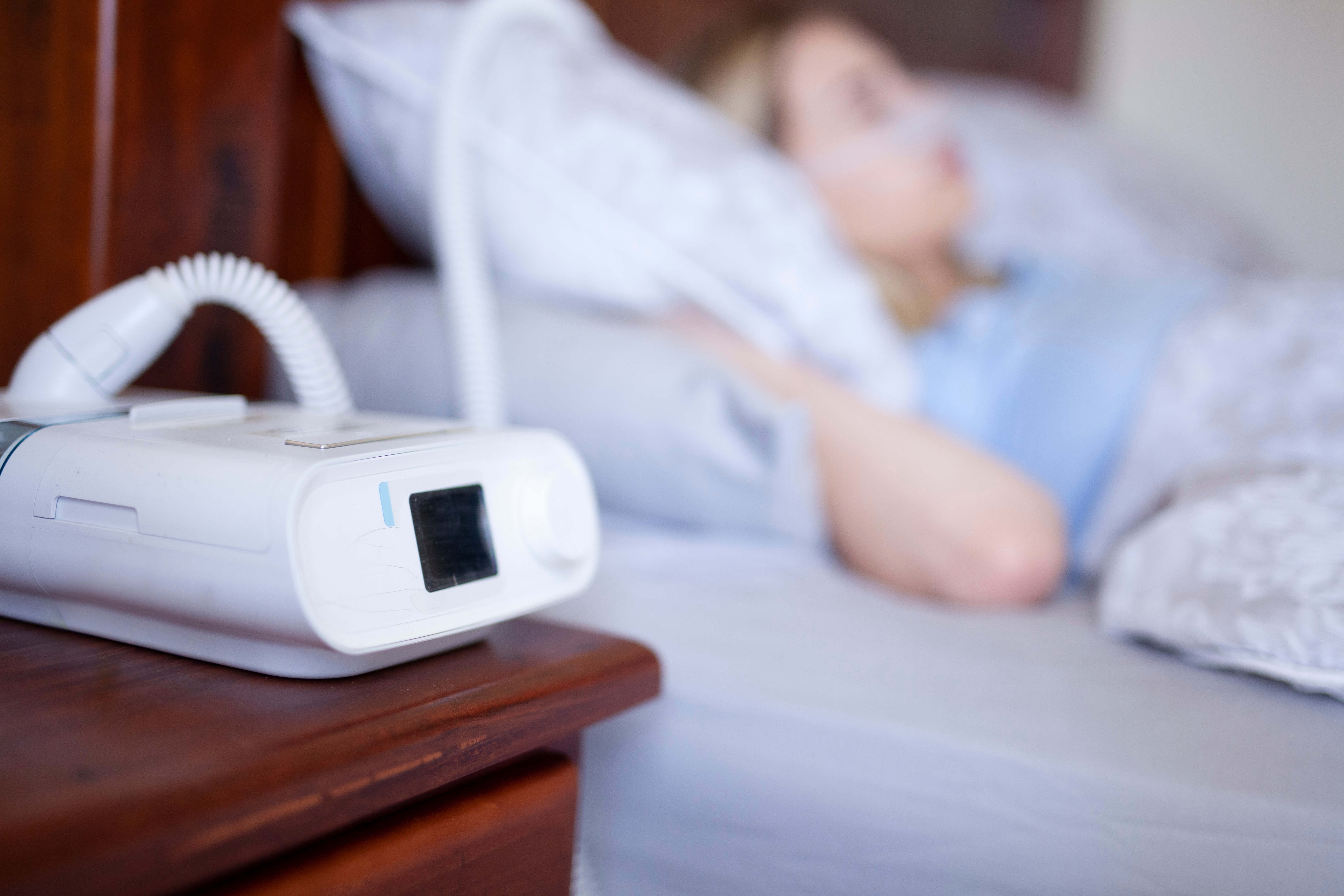 Person sleeping in bed with CPAP machine on nearby nightstand