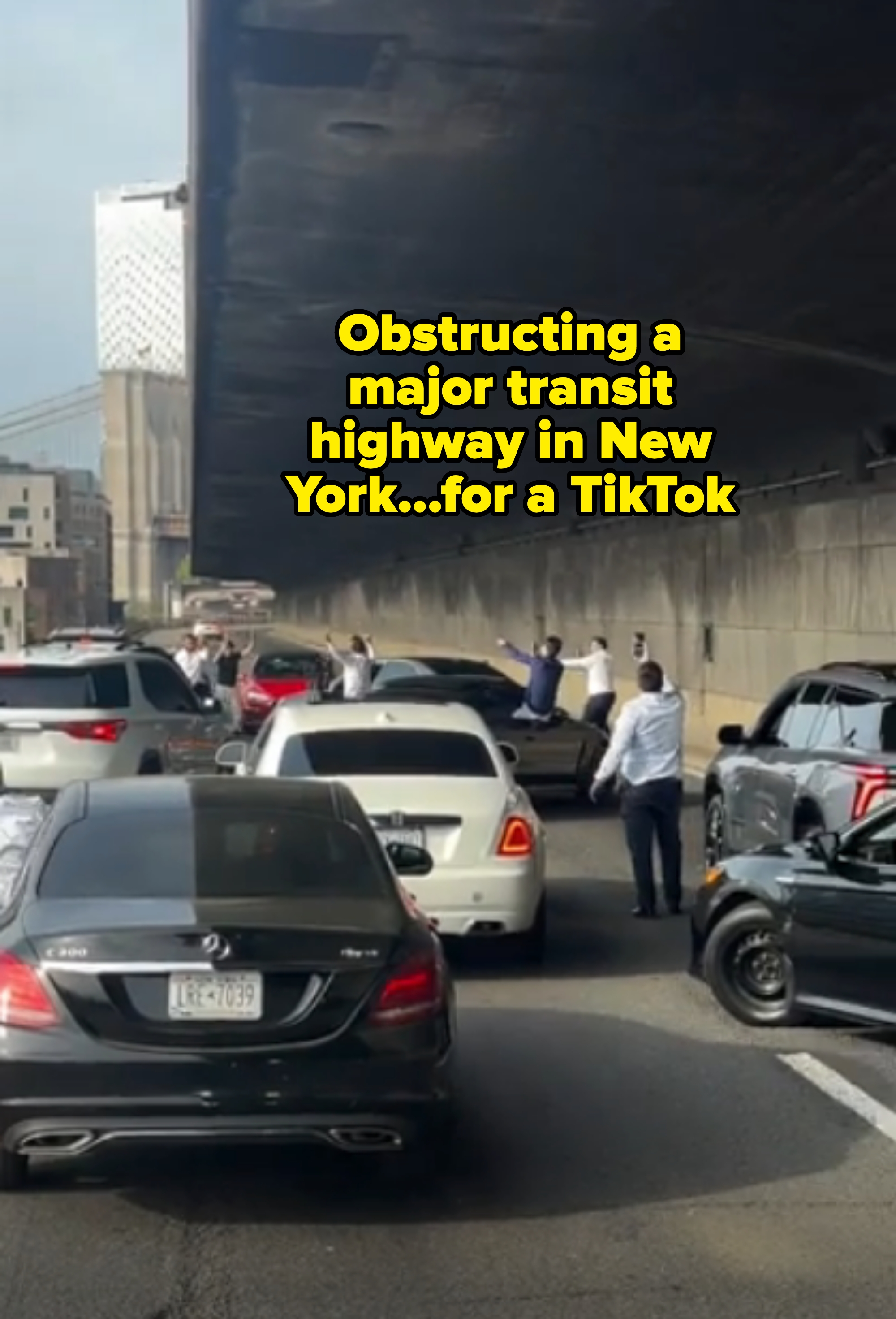 Traffic jam under a bridge with several drivers standing outside their cars, some taking photos or videos, captioned, &quot;Obstructing a major transit highway in New York...for a TikTok&quot;