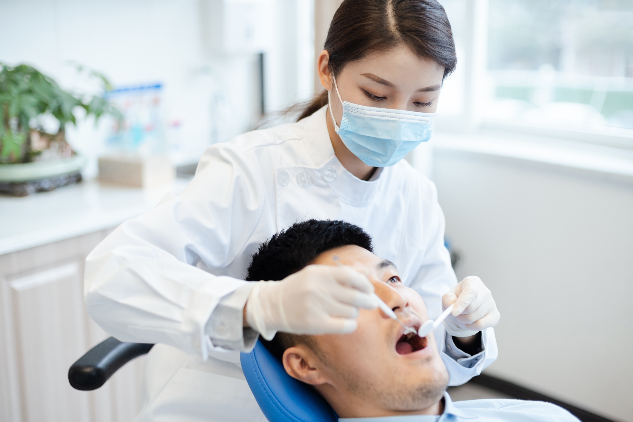 Dentist examines patient's teeth in a clinic, both wearing masks