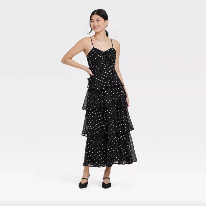 Person wearing a sleeveless, tiered polka-dot formal  and achromatic  heels, posing for a manner  article