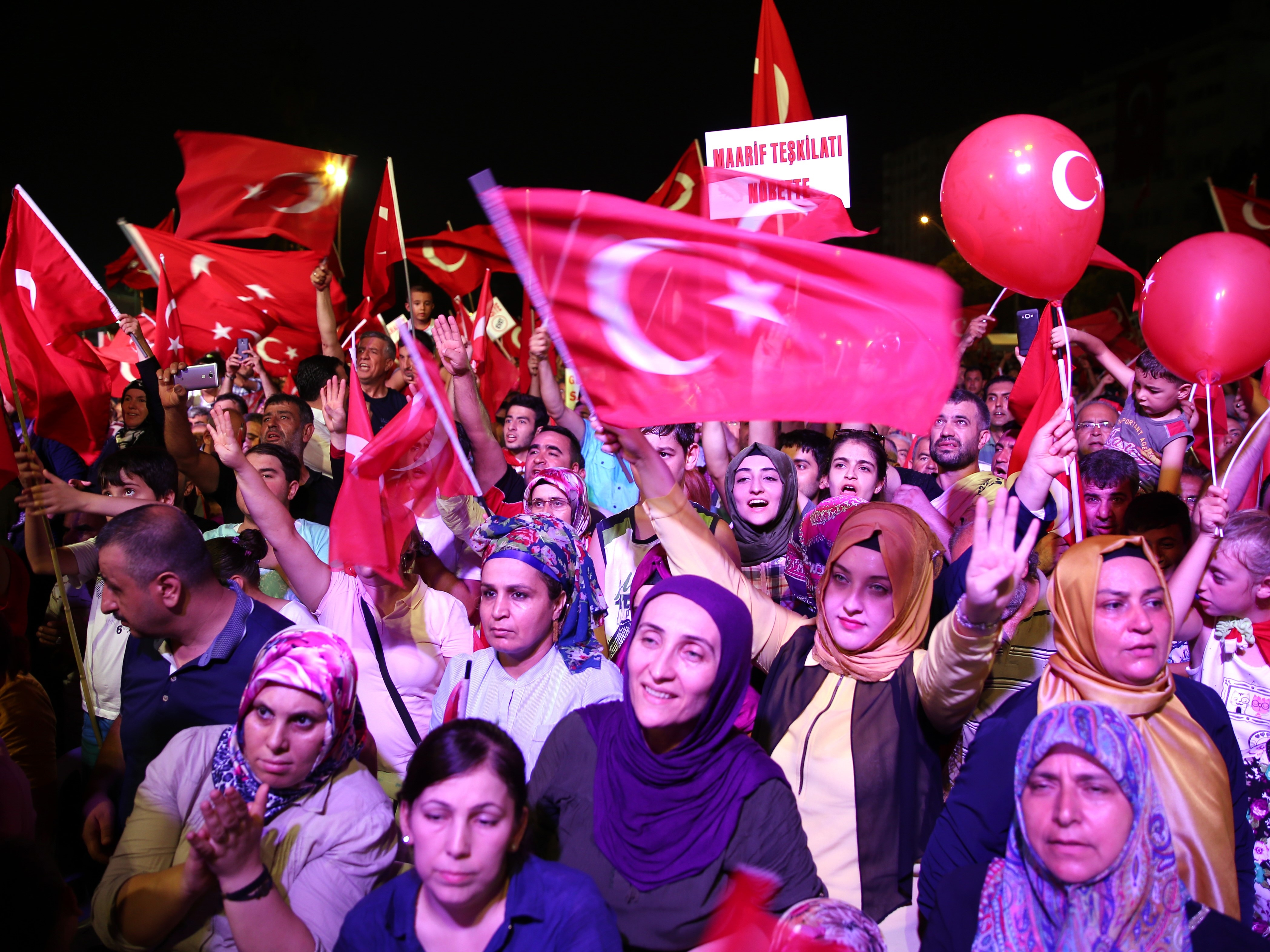 People waving Turkish flags and balloons, gathered in a lively crowd during a public event or celebration, showing enthusiasm and camaraderie