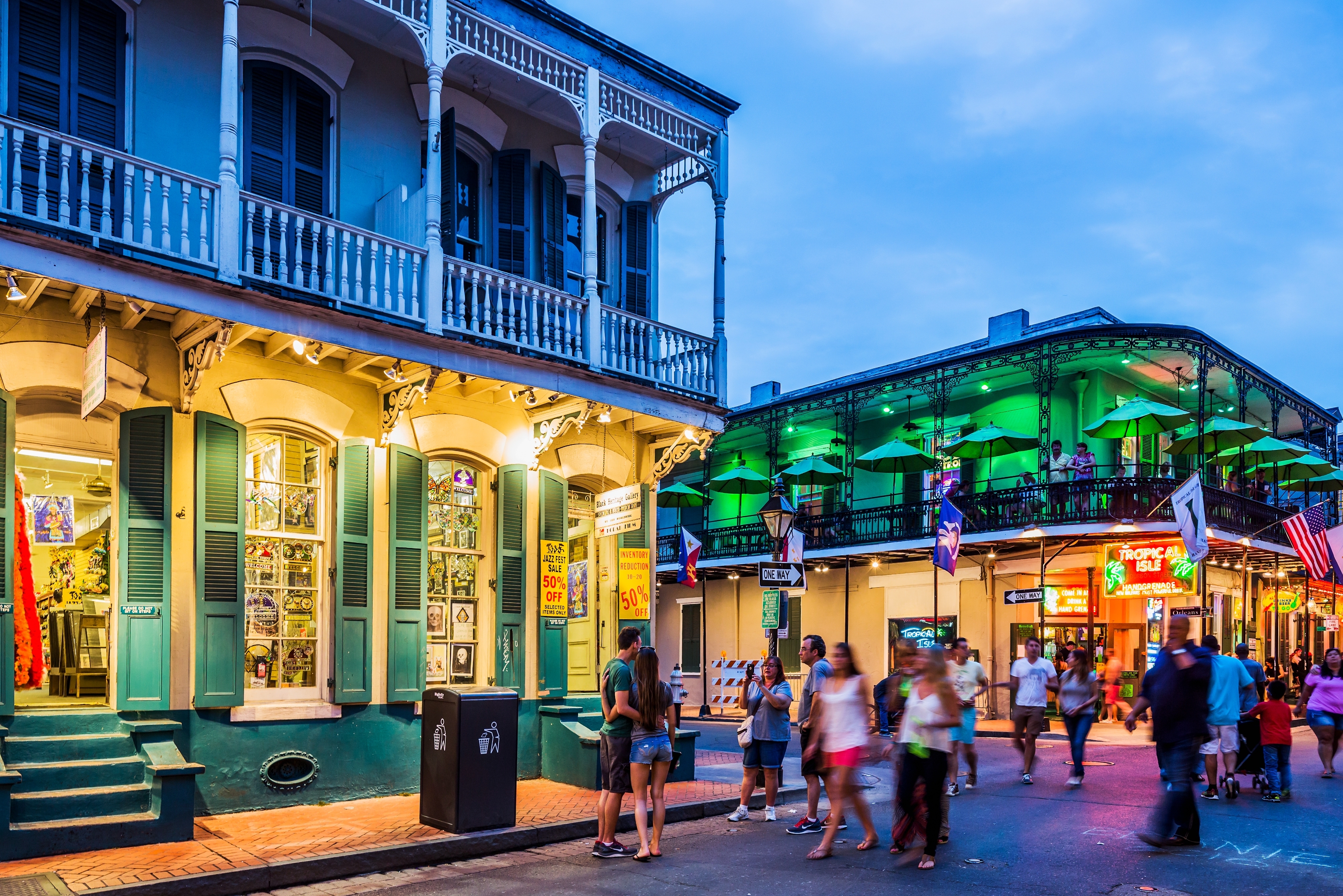 People walking on a lively street in New Orleans, featuring historic buildings with balconies and lit shopfronts