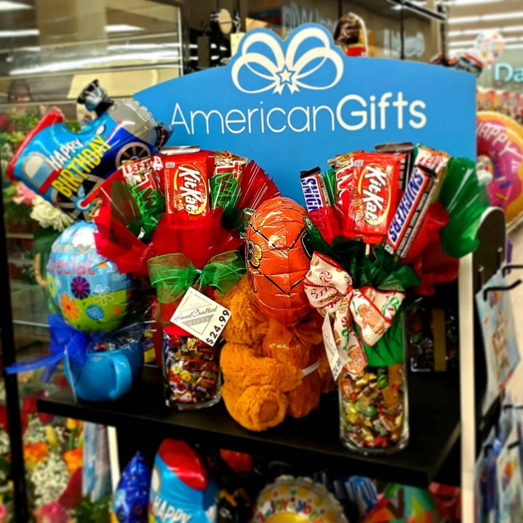 Gift display featuring candy bouquets in glass jars with assorted chocolates and sweets, surrounded by colorful balloons