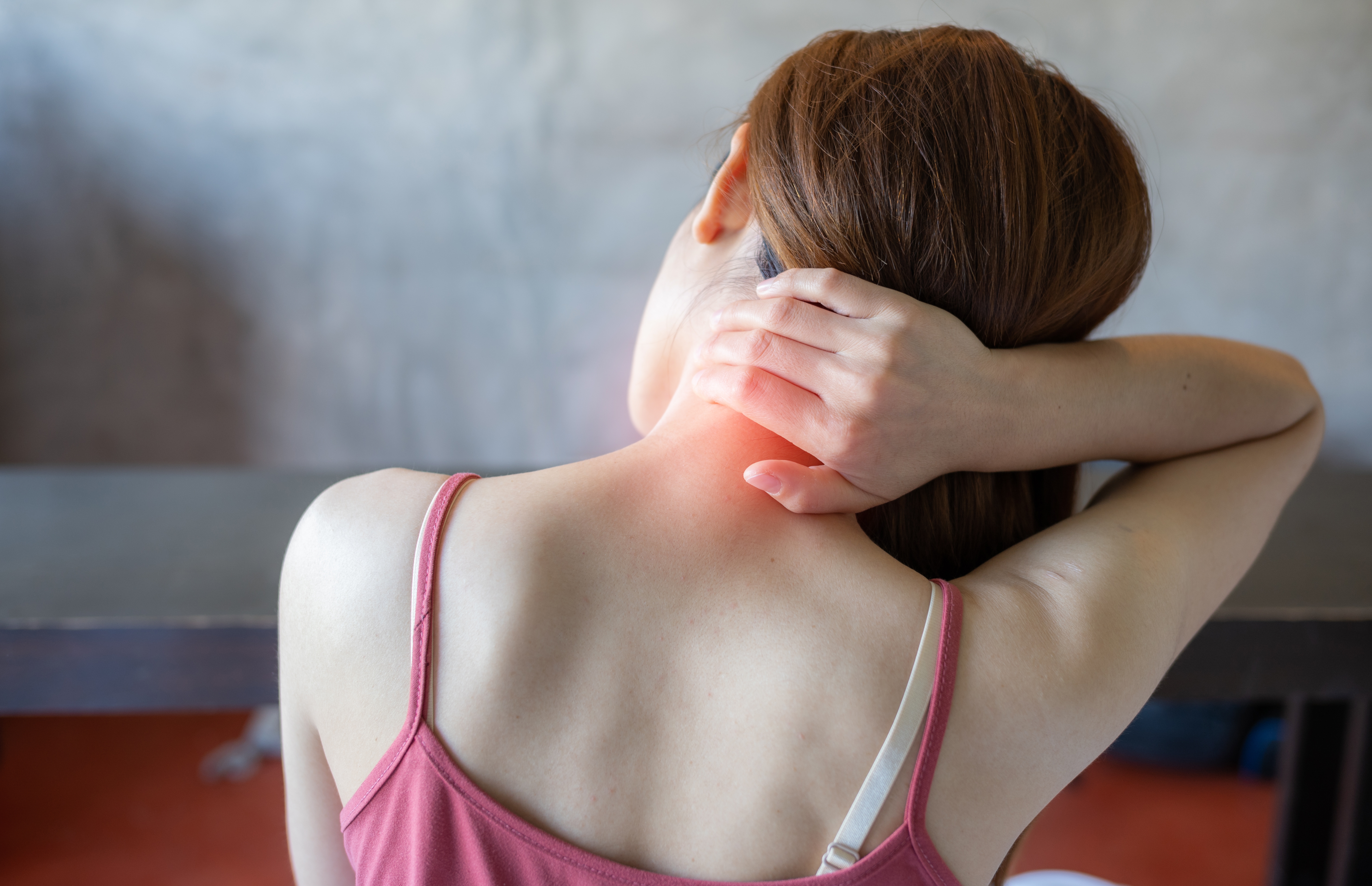 Person rubbing their neck with one hand, wearing a sleeveless top, indicating discomfort or tension in the neck area