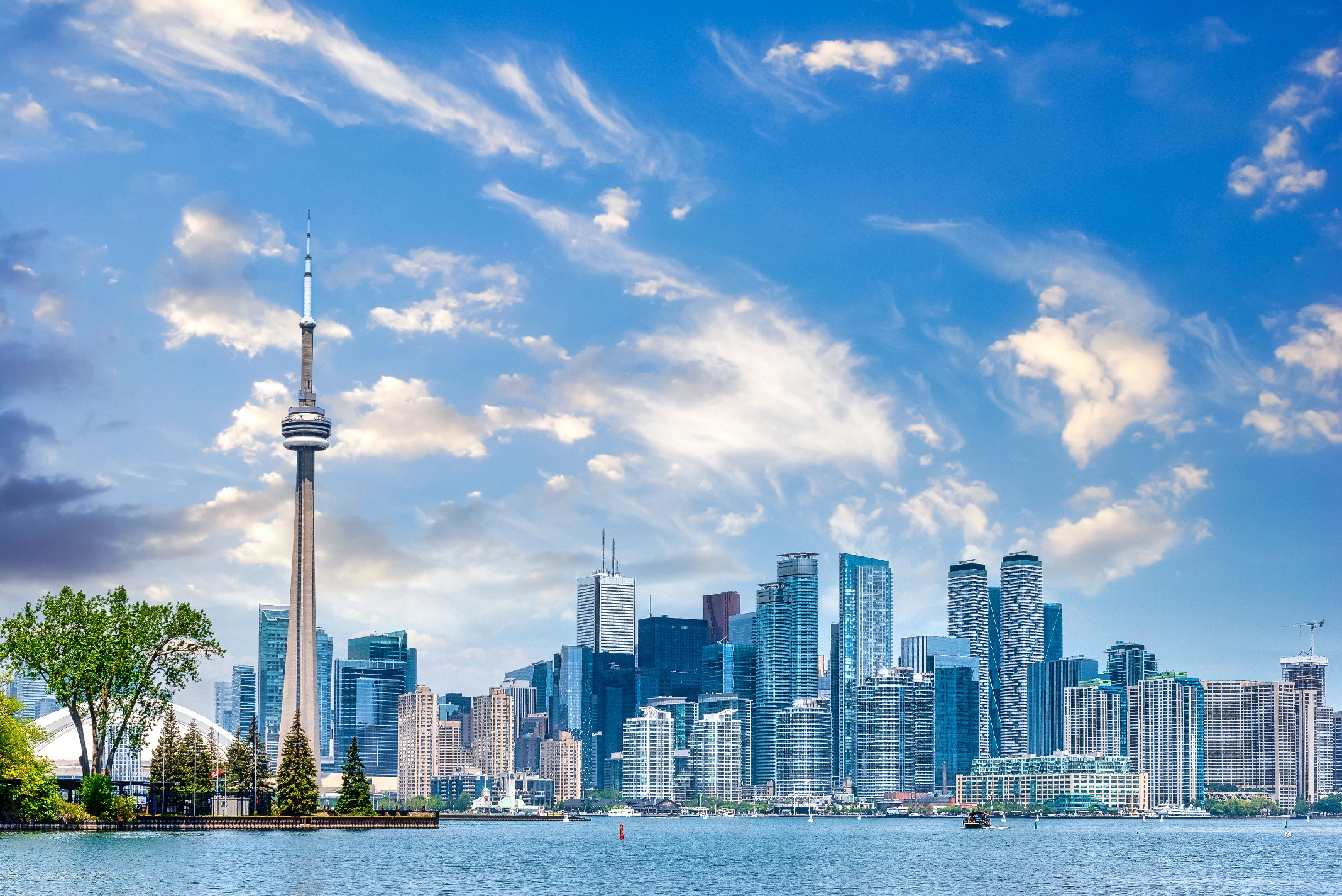 Toronto skyline with CN Tower and lake in the foreground under cloudy sky, showcasing the cityscape's modern architecture