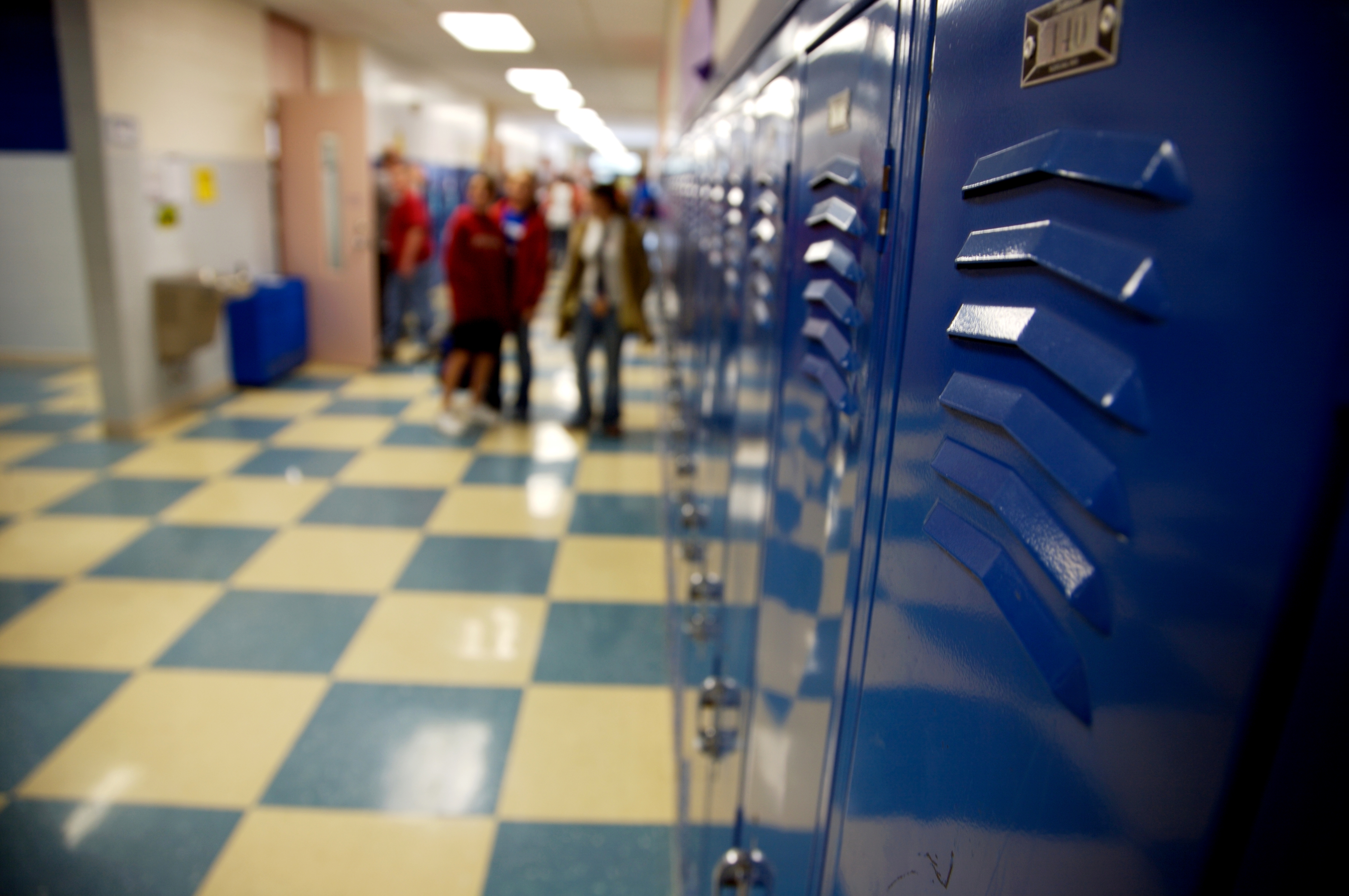 School hallway with closed lockers on the right and a group of students walking in the background