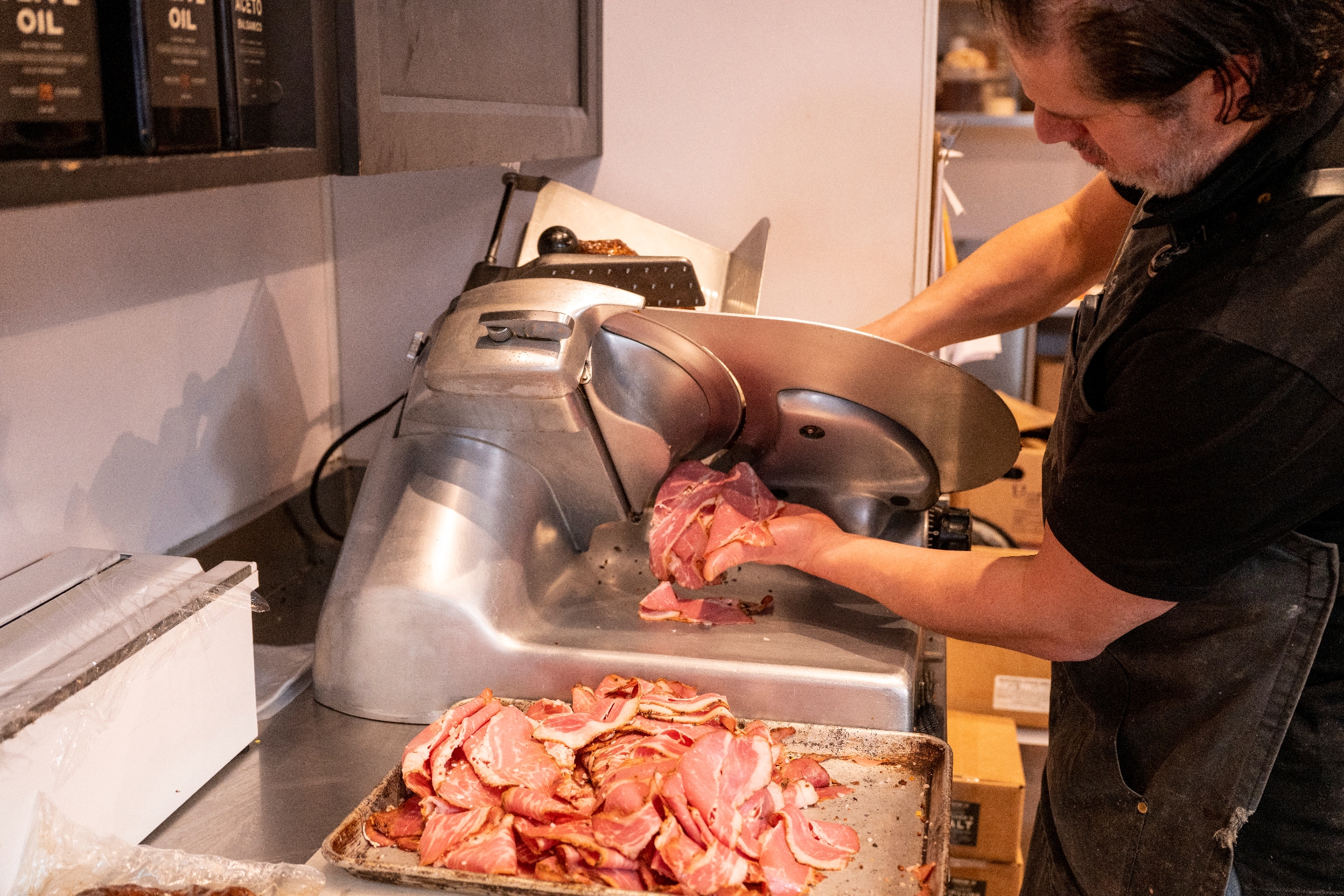 Person slicing meat in a deli with a meat slicer; sliced pieces are on a tray