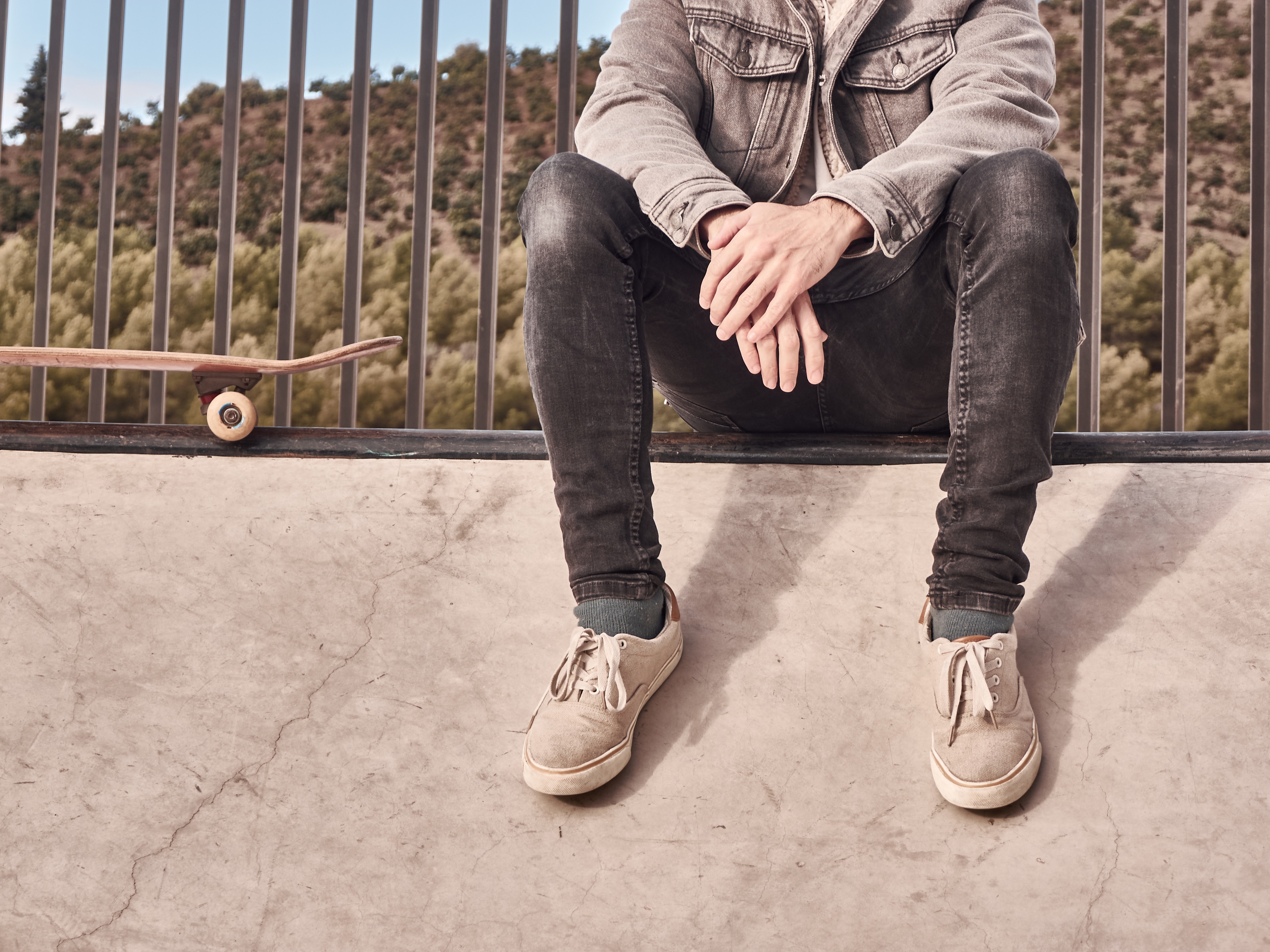 Person sits on skatepark edge, in casual jeans and a denim jacket, skateboard nearby
