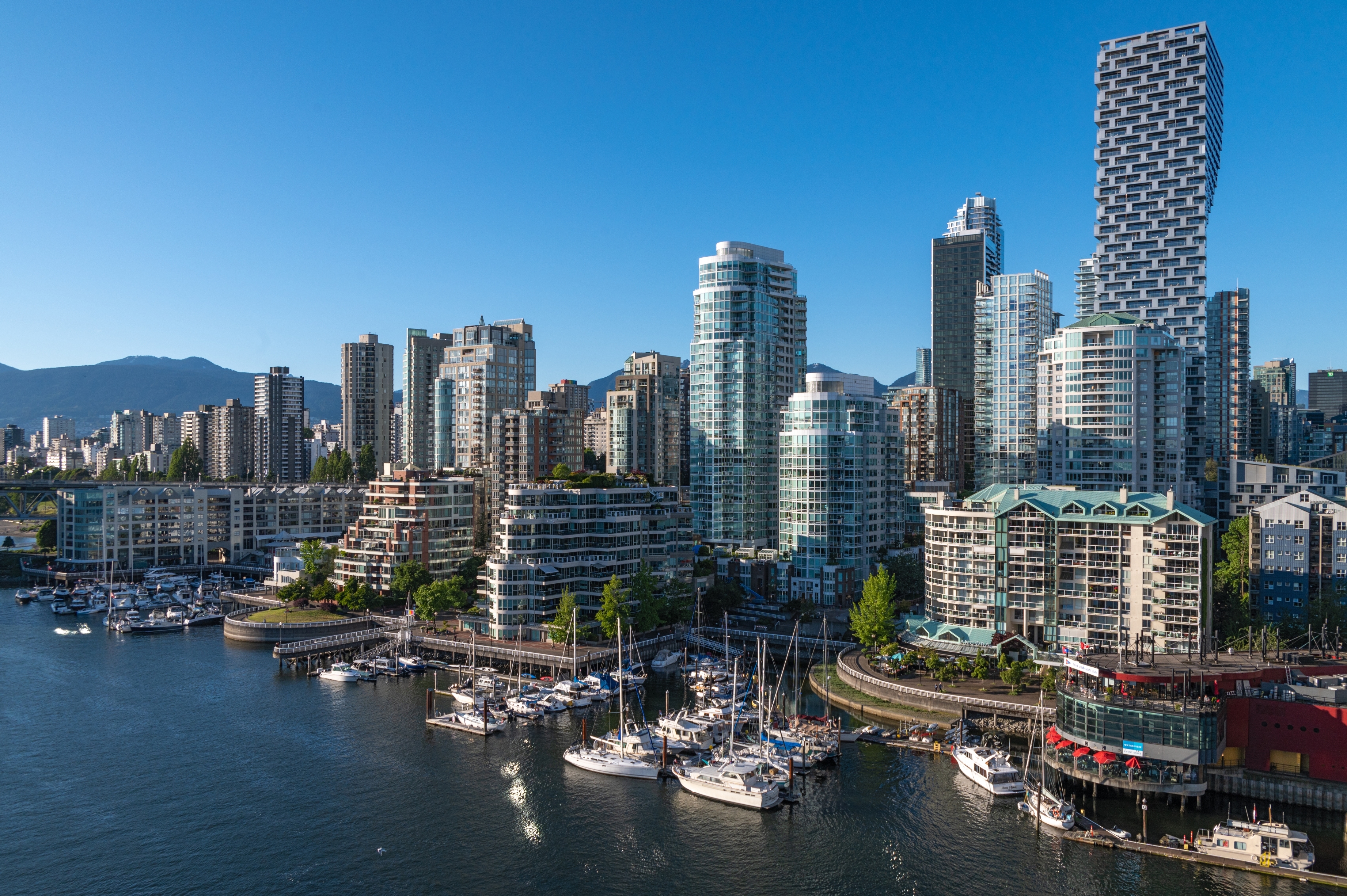 Vancouver skyline with modern high-rises along the waterfront, and boats docked in the marina, under a clear blue sky