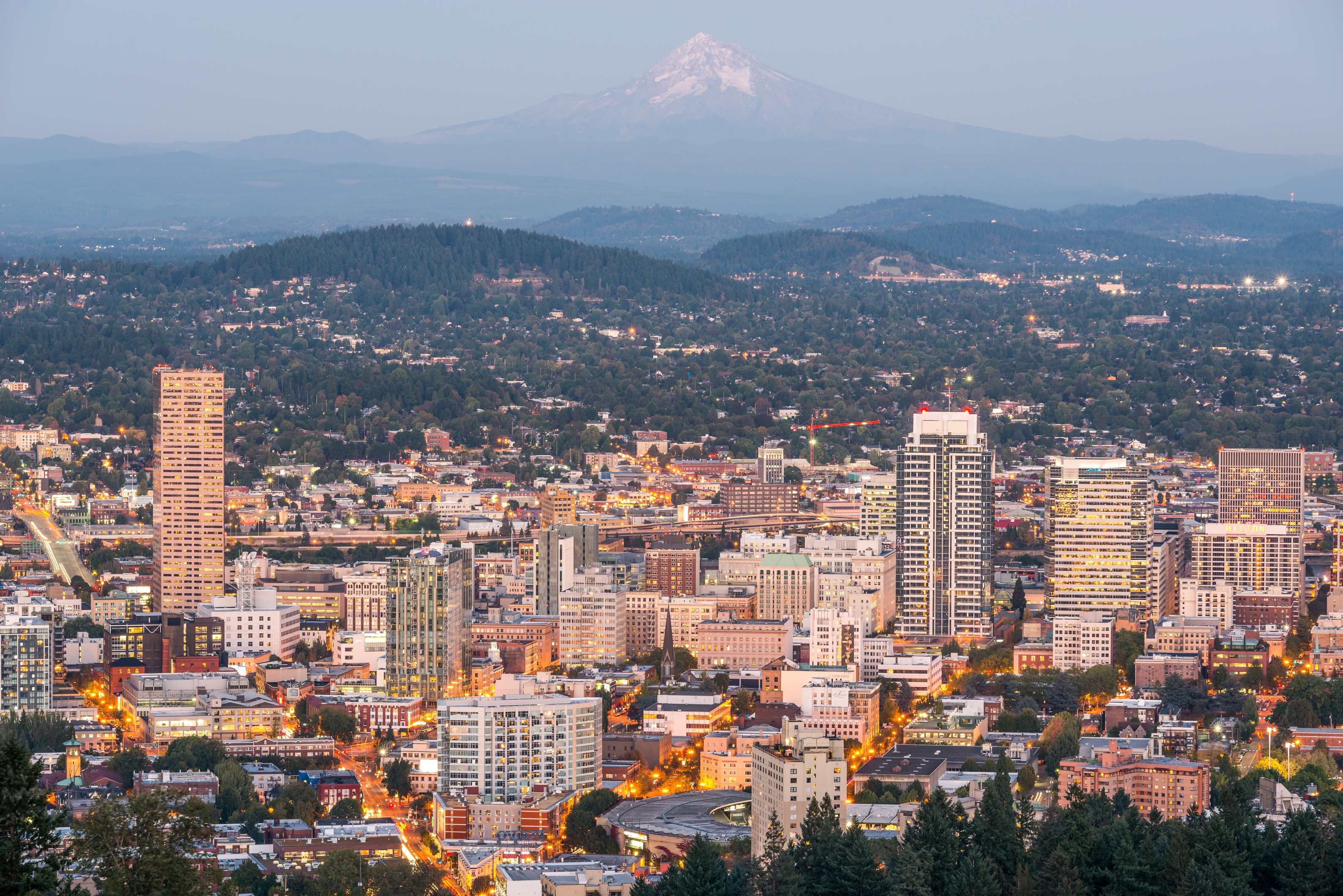 Cityscape of Portland with skyscrapers in the foreground and a distant mountain peak in the background during evening twilight