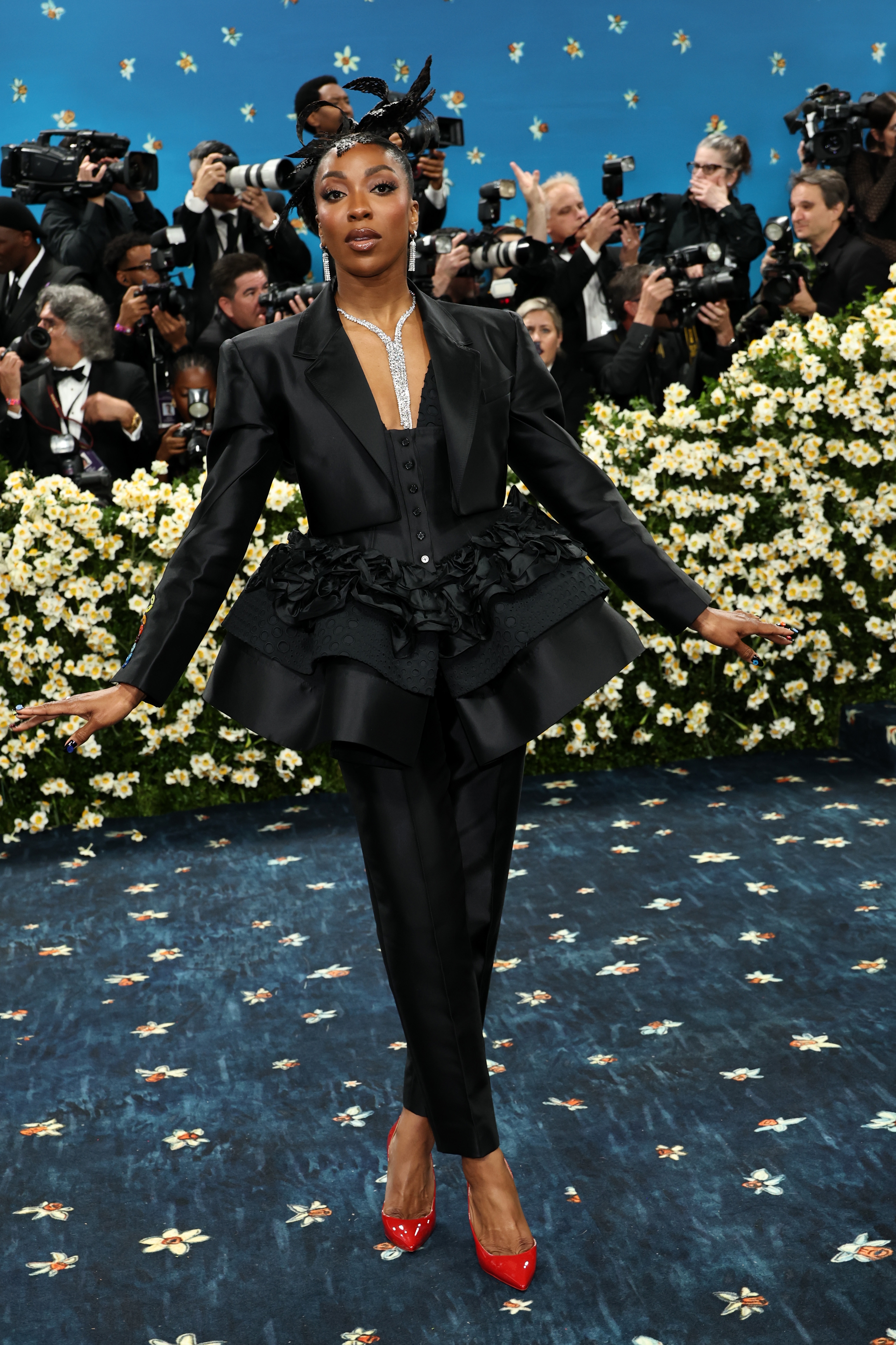 Person in elaborate black tuxedo dress on red carpet with photographers in background