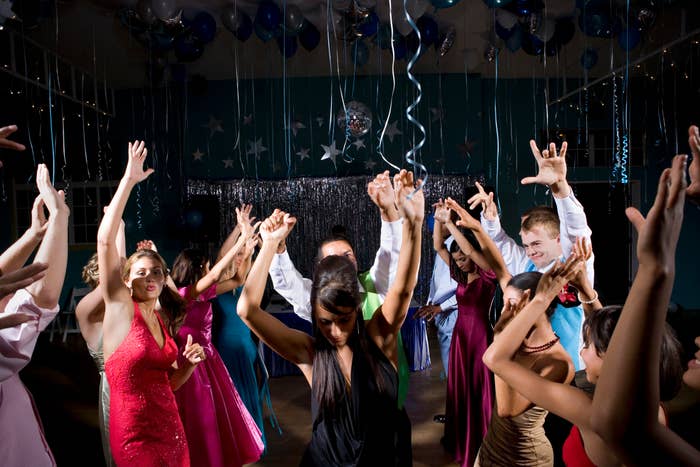People dancing energetically at a prom-like event, dressed in formal attire
