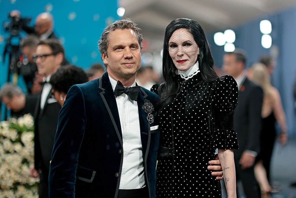 Harry in a velvet suit and bow tie stands with Jill wearing a polka dot dress and veiled headpiece