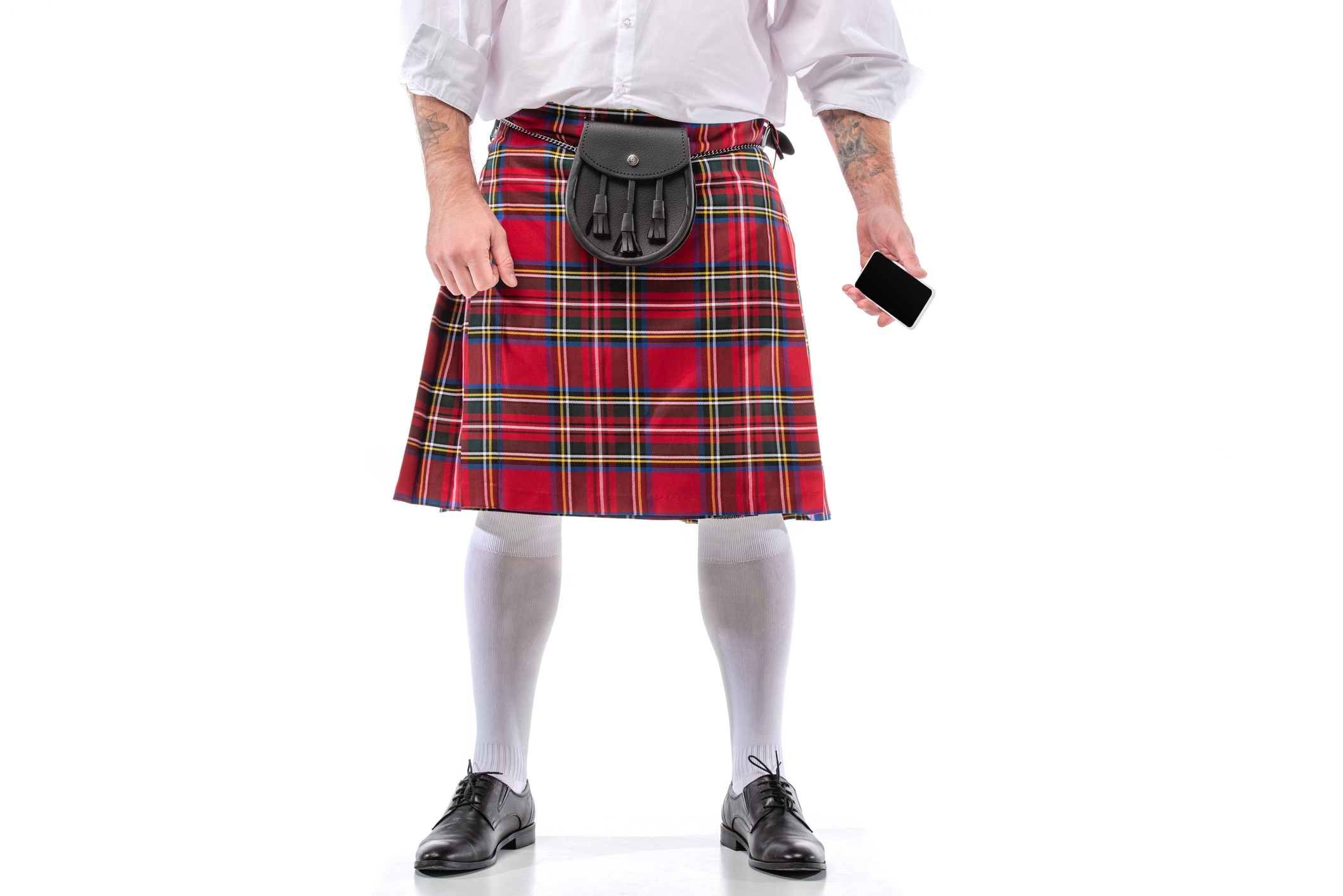 Person wearing a plaid kilt, white shirt, and holding a smartphone
