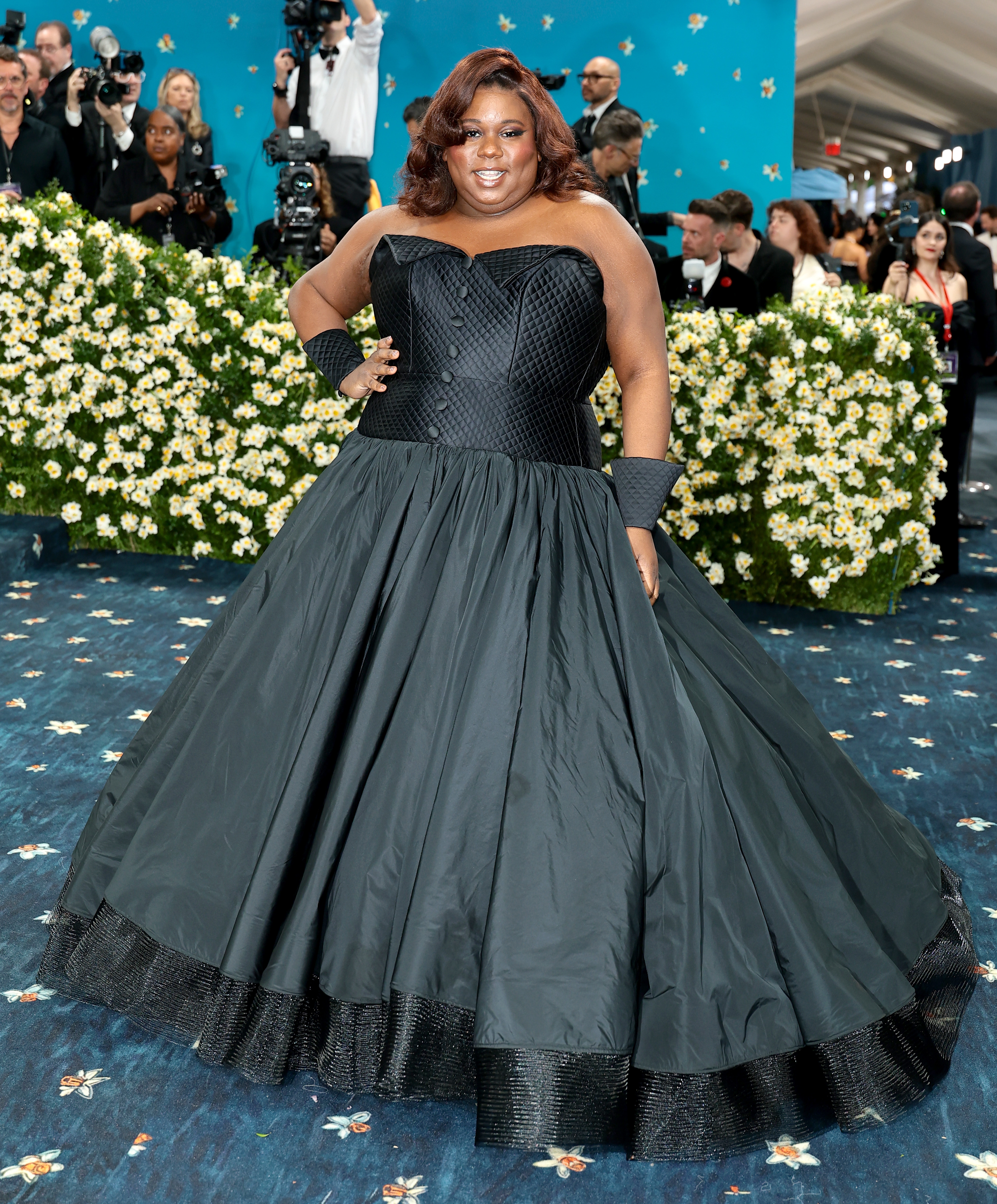 Person in a black textured ball gown poses confidently on a floral-decorated walkway at a formal event