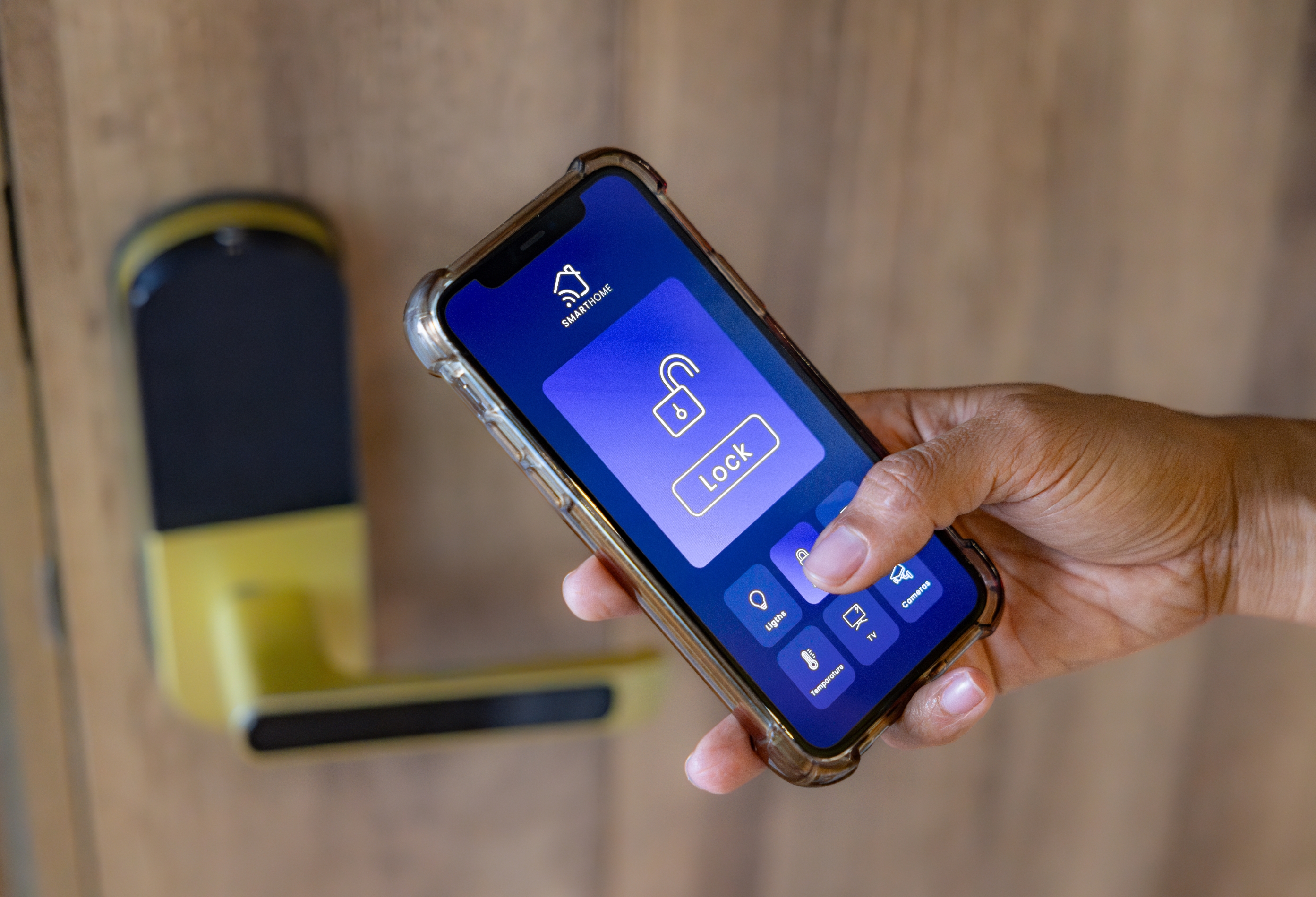 Hand holding a smartphone with a smart lock app screen unlocking a door lock