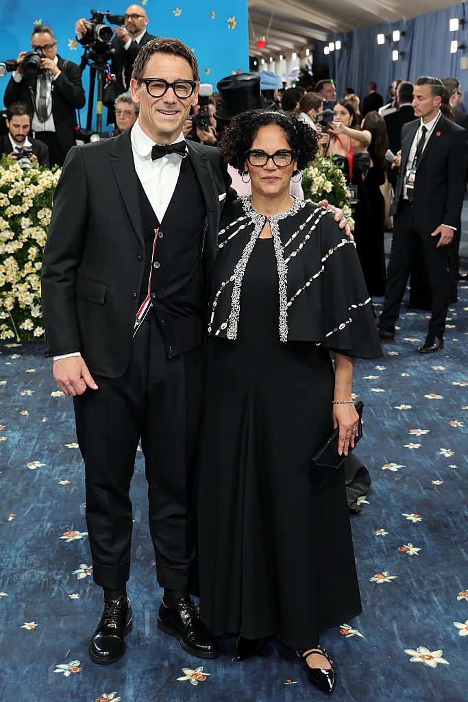 Carl wears a tuxedo with a bow tie, and Monica wears a dress with a jeweled cape