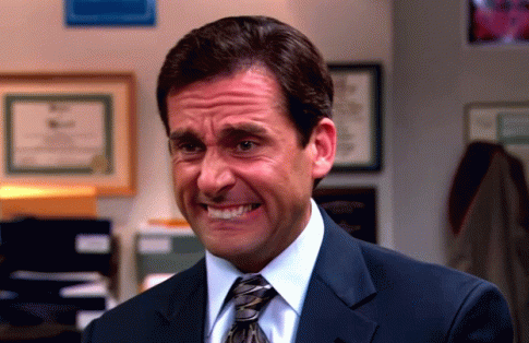 A person in a suit grimaces awkwardly, appearing uncomfortable in an office setting