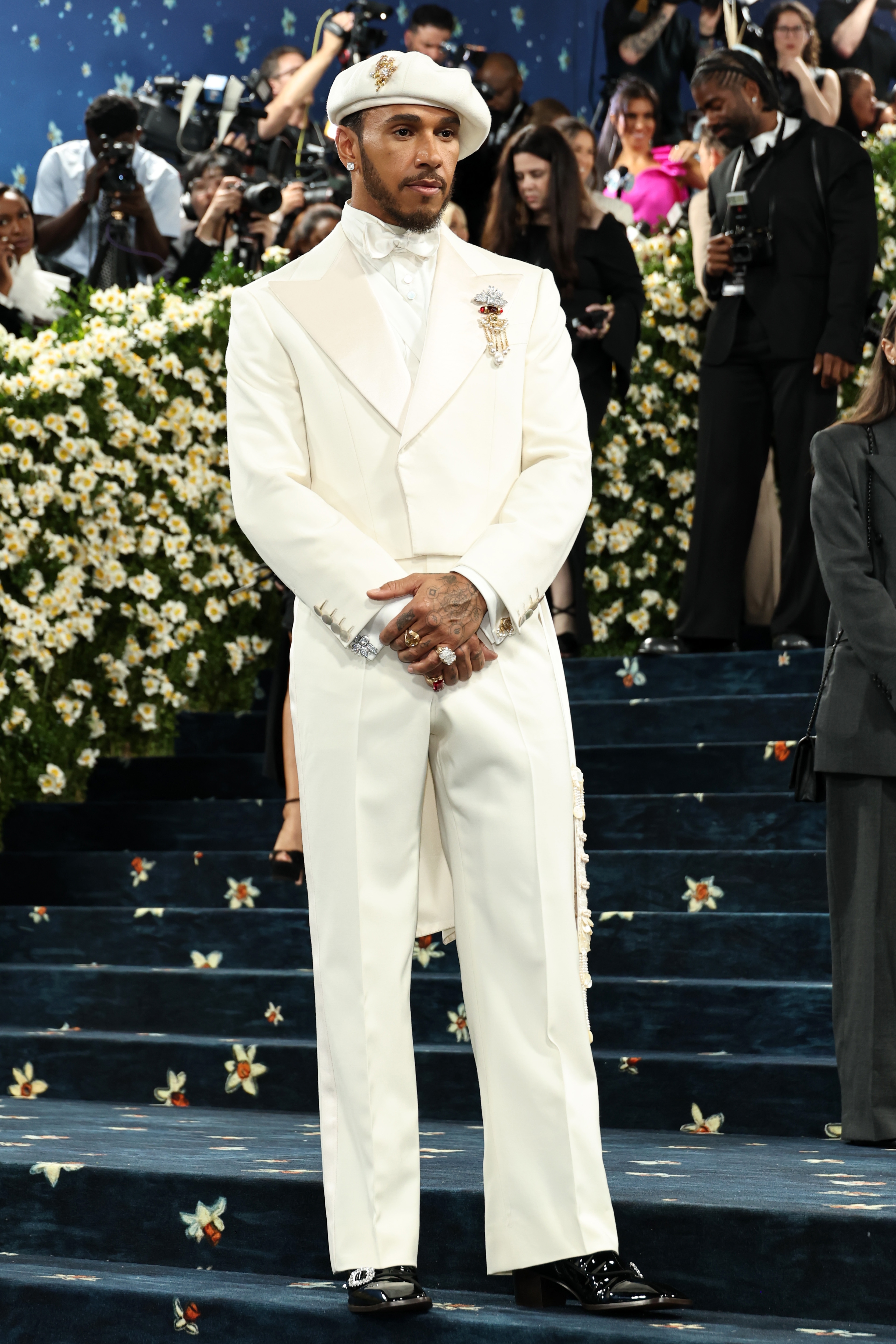 Man in elegant tailored suit with unique accessories on a red carpet, surrounded by photographers and guests