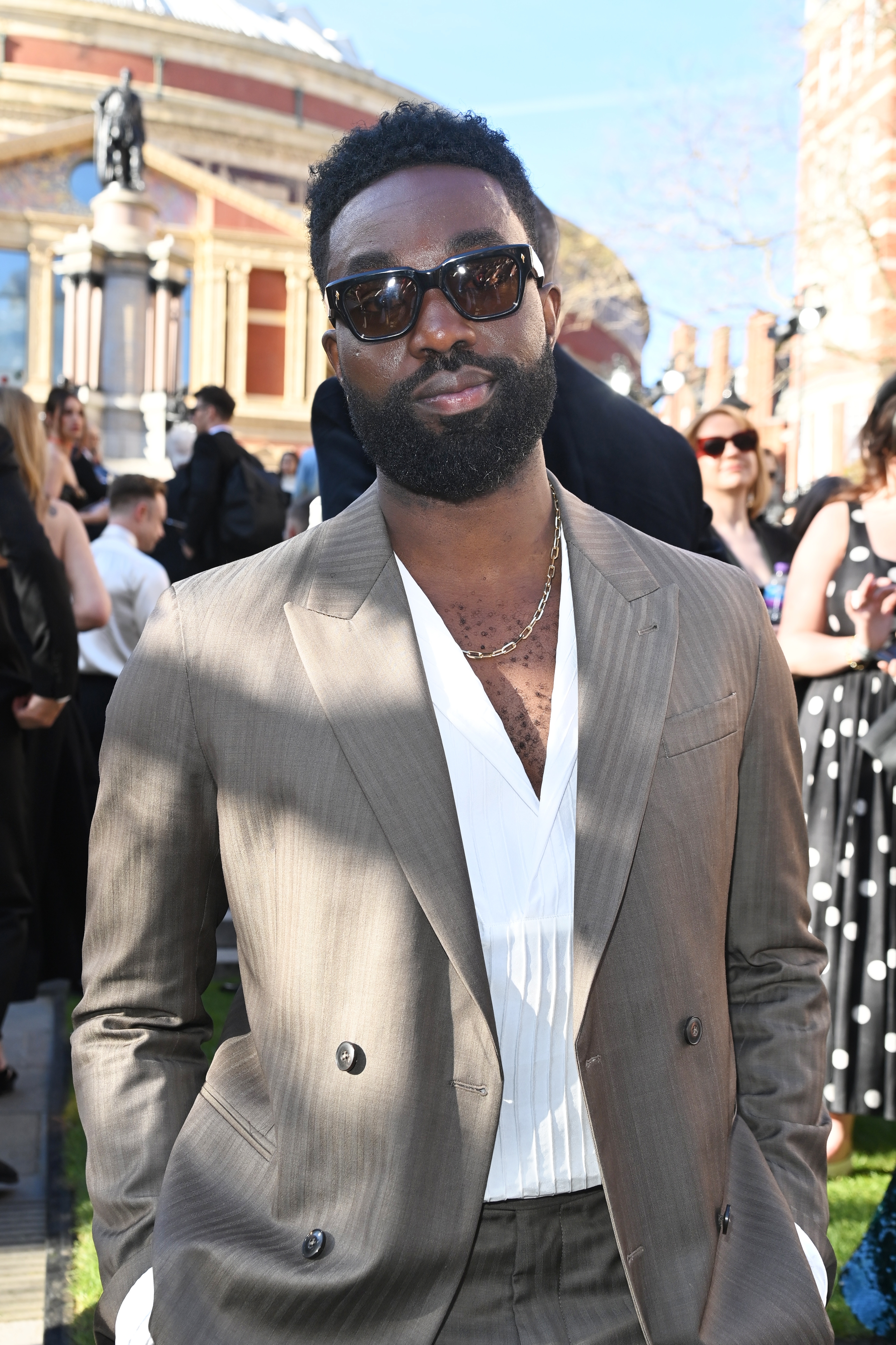 Paapa Esseidu in a double-breasted suit and sunglasses posing outdoors at a formal event