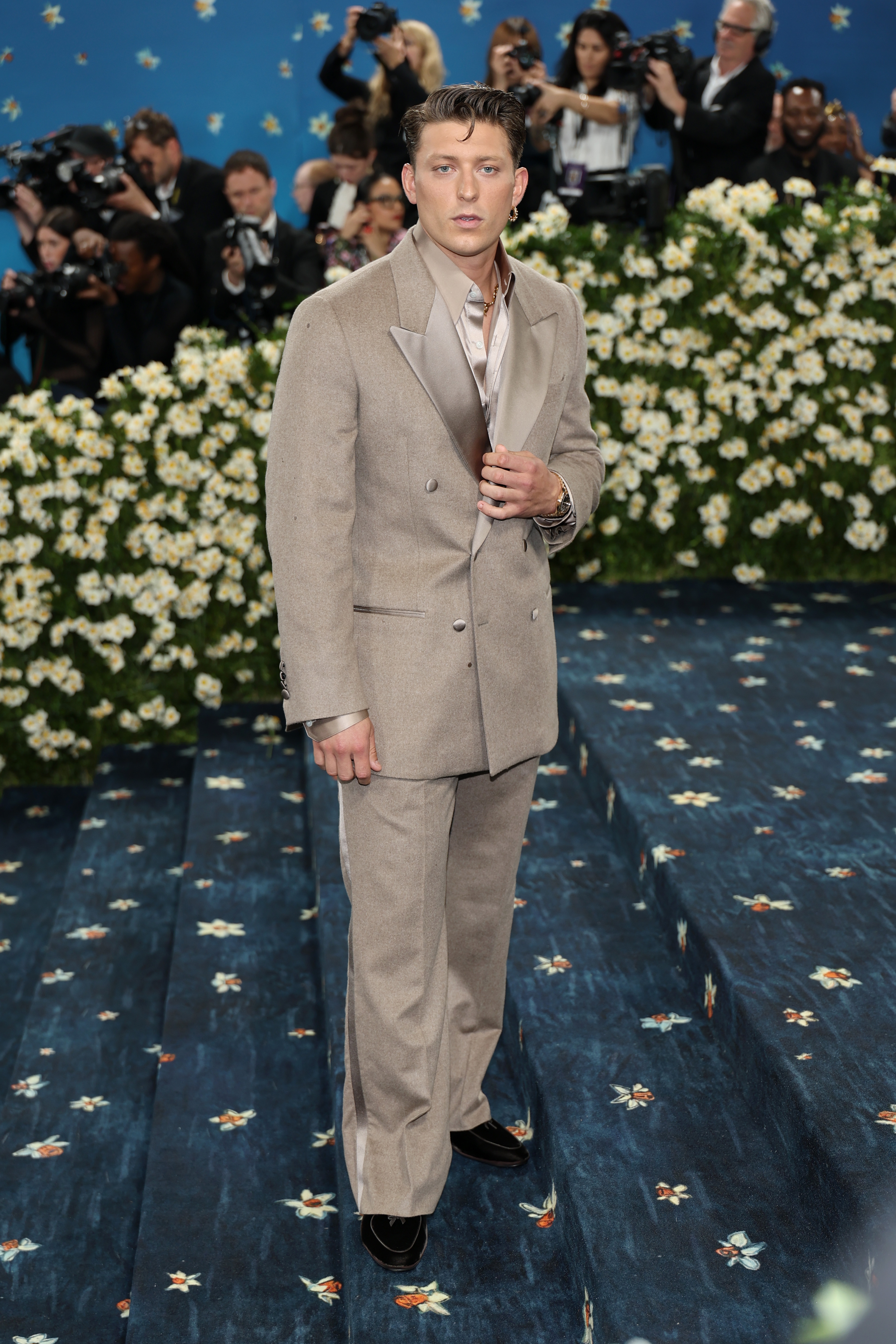 Person in a tailored suit stands on a floral-patterned carpet, posing for photographers