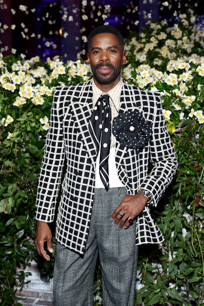 Colman Domingo in checkered suit with floral lapel stands in front of flower backdrop