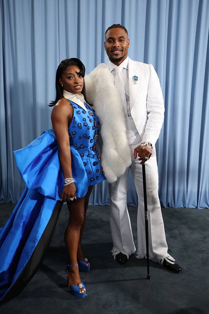 Simone in an embellished dress with a train, Jonathan in a suit with fur trim, holding a cane