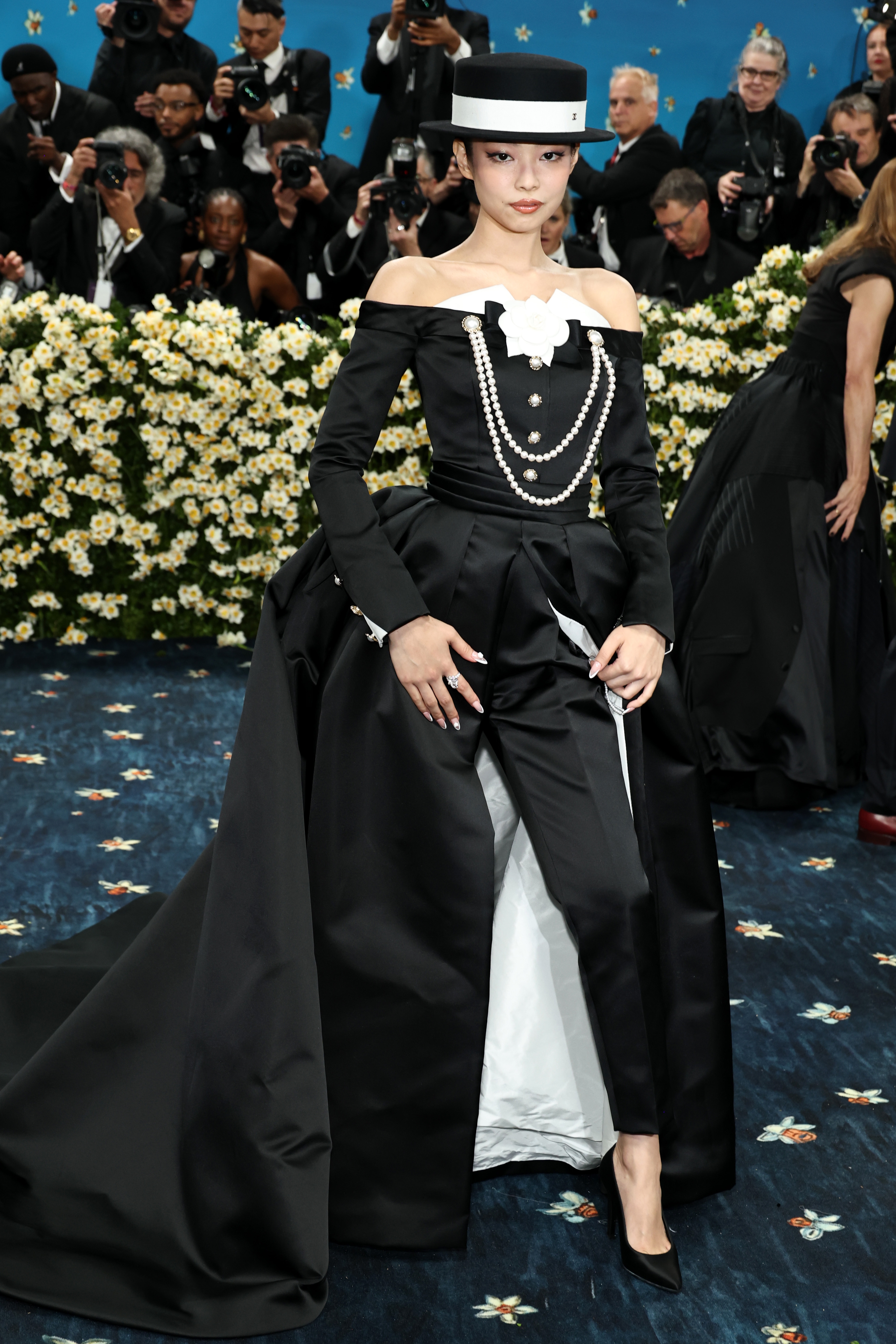 Celebrity in a black off-shoulder gown with pearls and a white bow, wearing a matching hat