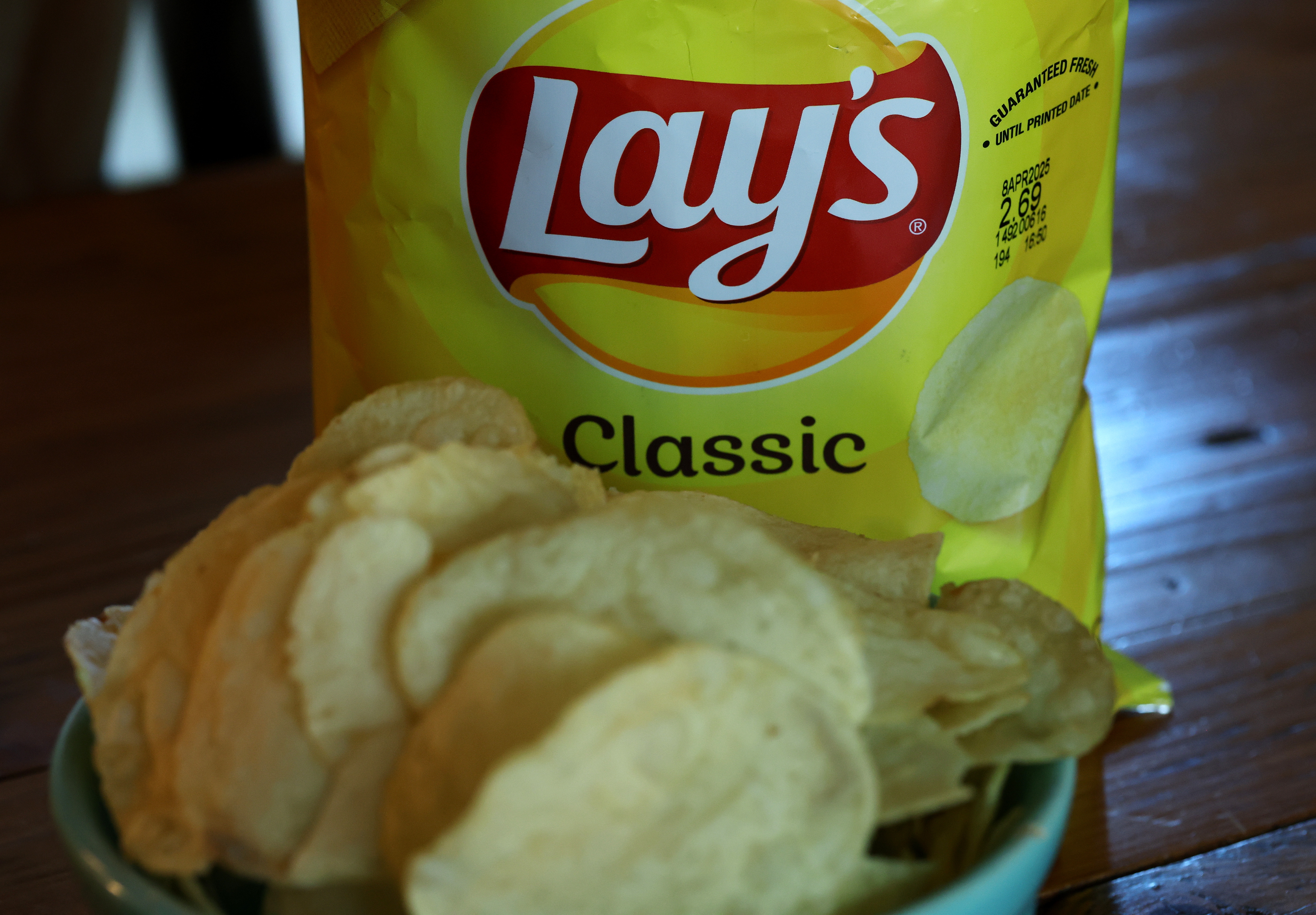 Bag of Lay's Classic potato chips next to a bowl filled with the same chips on a wooden surface