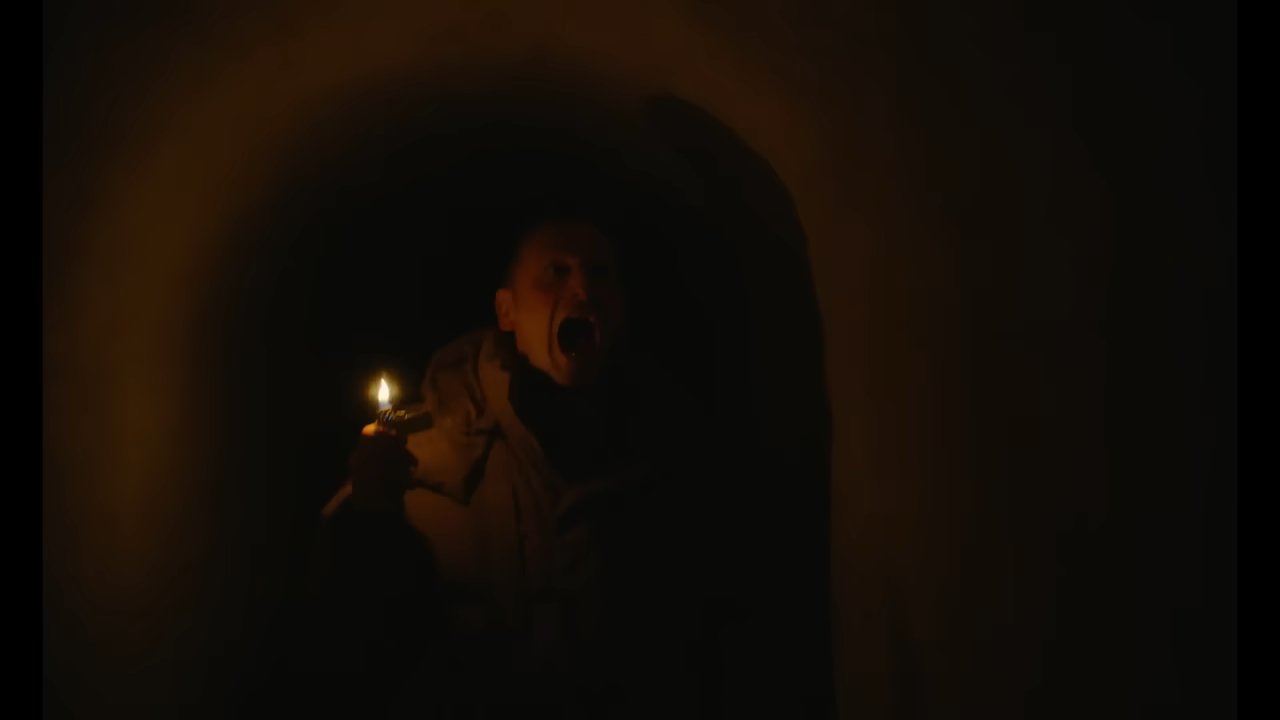 Person in dark tunnel holding a lit candle, mouth open in an expression of fear or shock