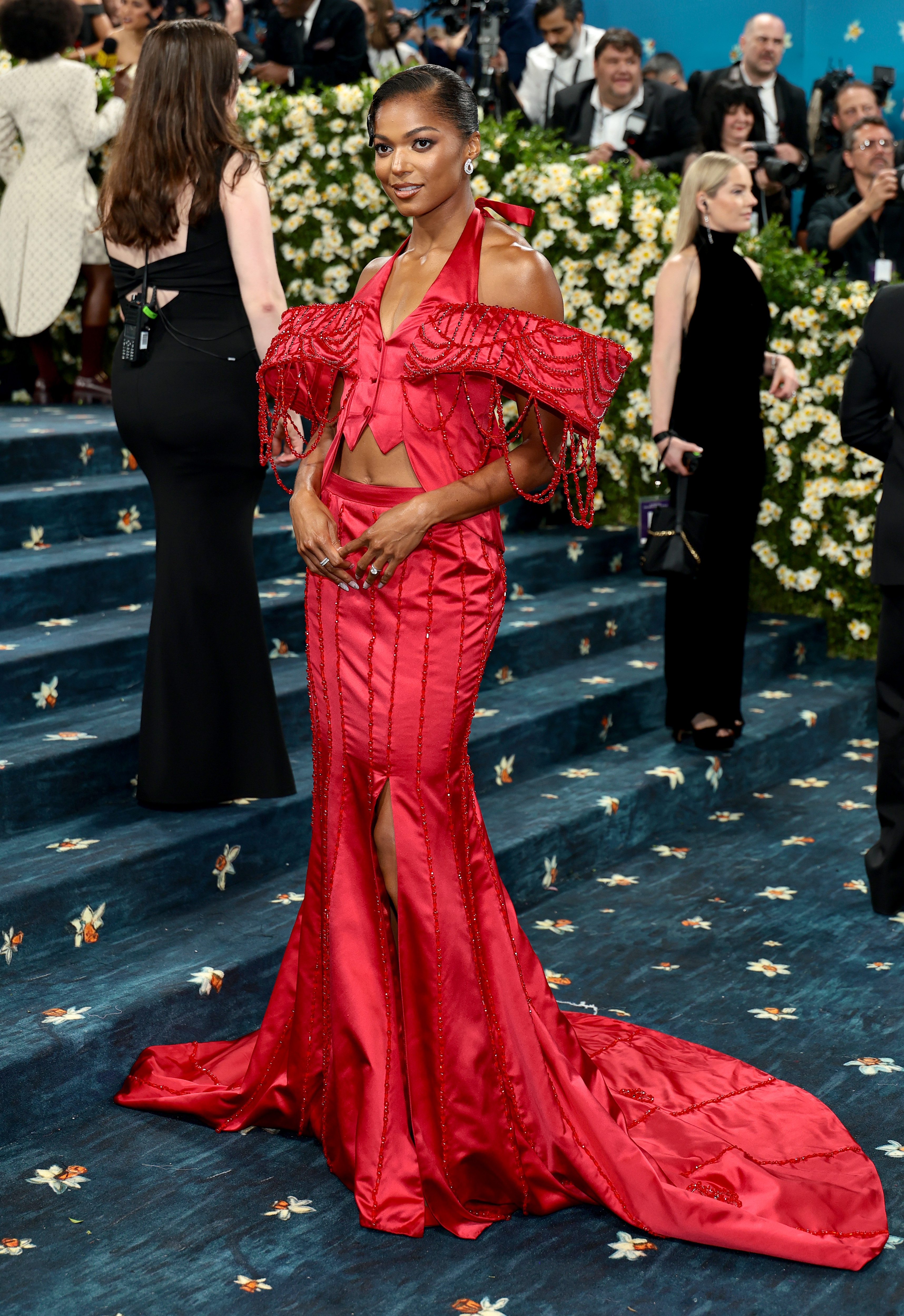 A person on the red carpet wearing an elegant, off-shoulder gown with intricate detailing and a long train