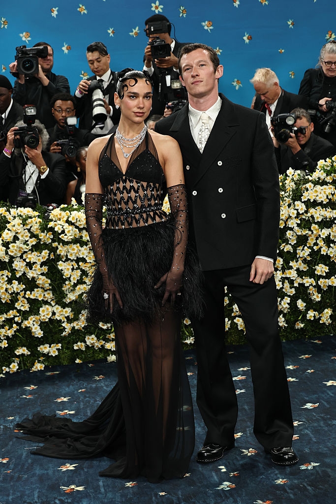 Dua wears a feathered gown with sheer elements; Callum wears a classic suit