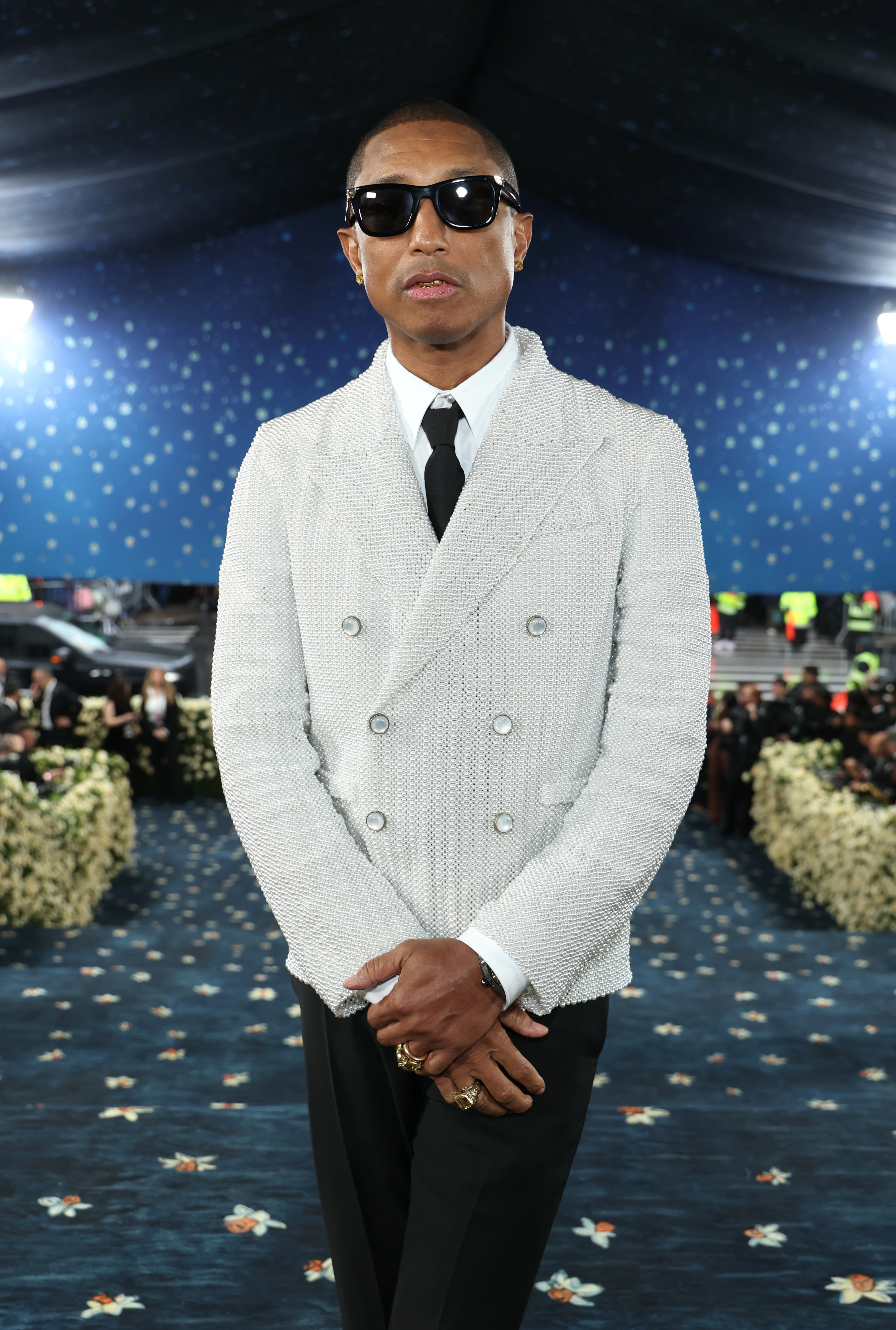 Pharrell in stylish double-breasted suit with sunglasses, standing in a starry-themed venue