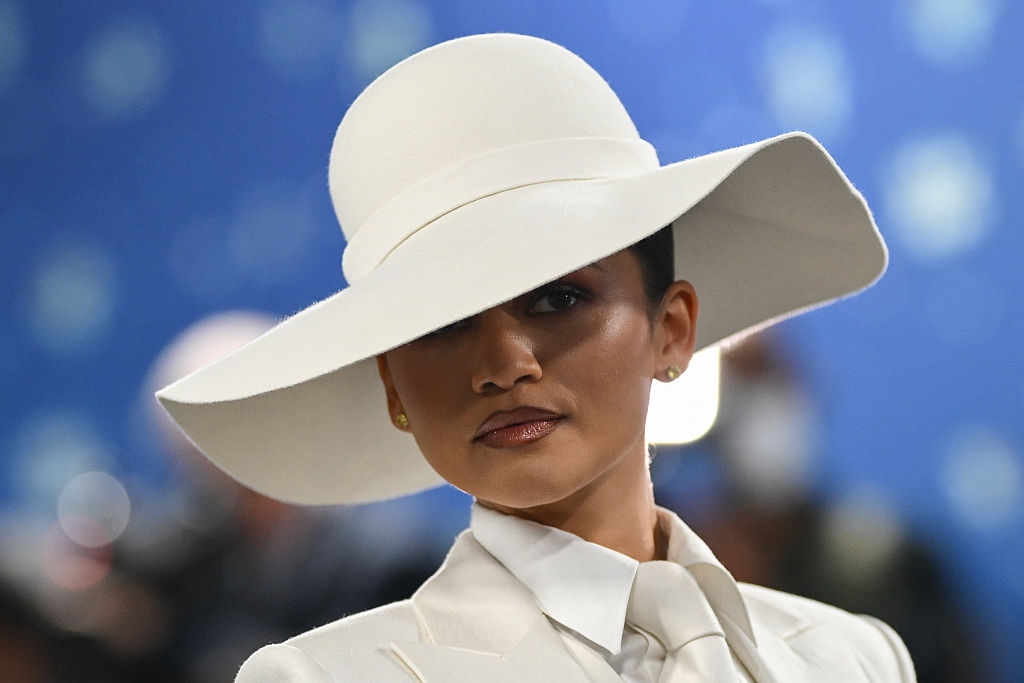 Person in elegant wide-brimmed hat and formal attire, looks poised at an event