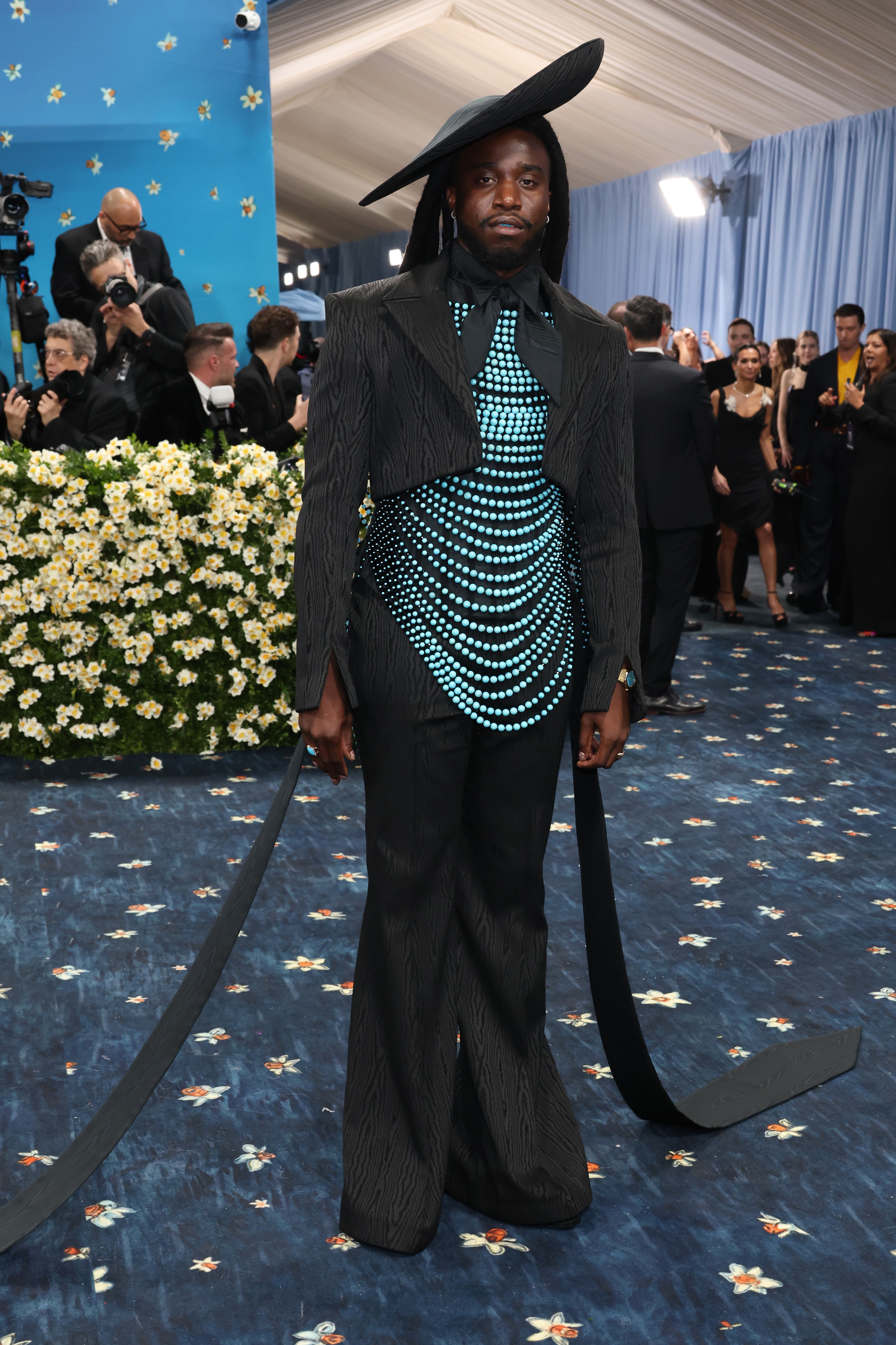 Celebrity in avant-garde outfit with wide-brim hat and structured design on the blue carpet at a formal event