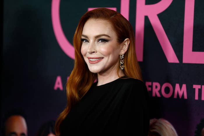 A person on a red carpet wearing elegant, long earrings and a sleek black outfit, smiling at a film premiere