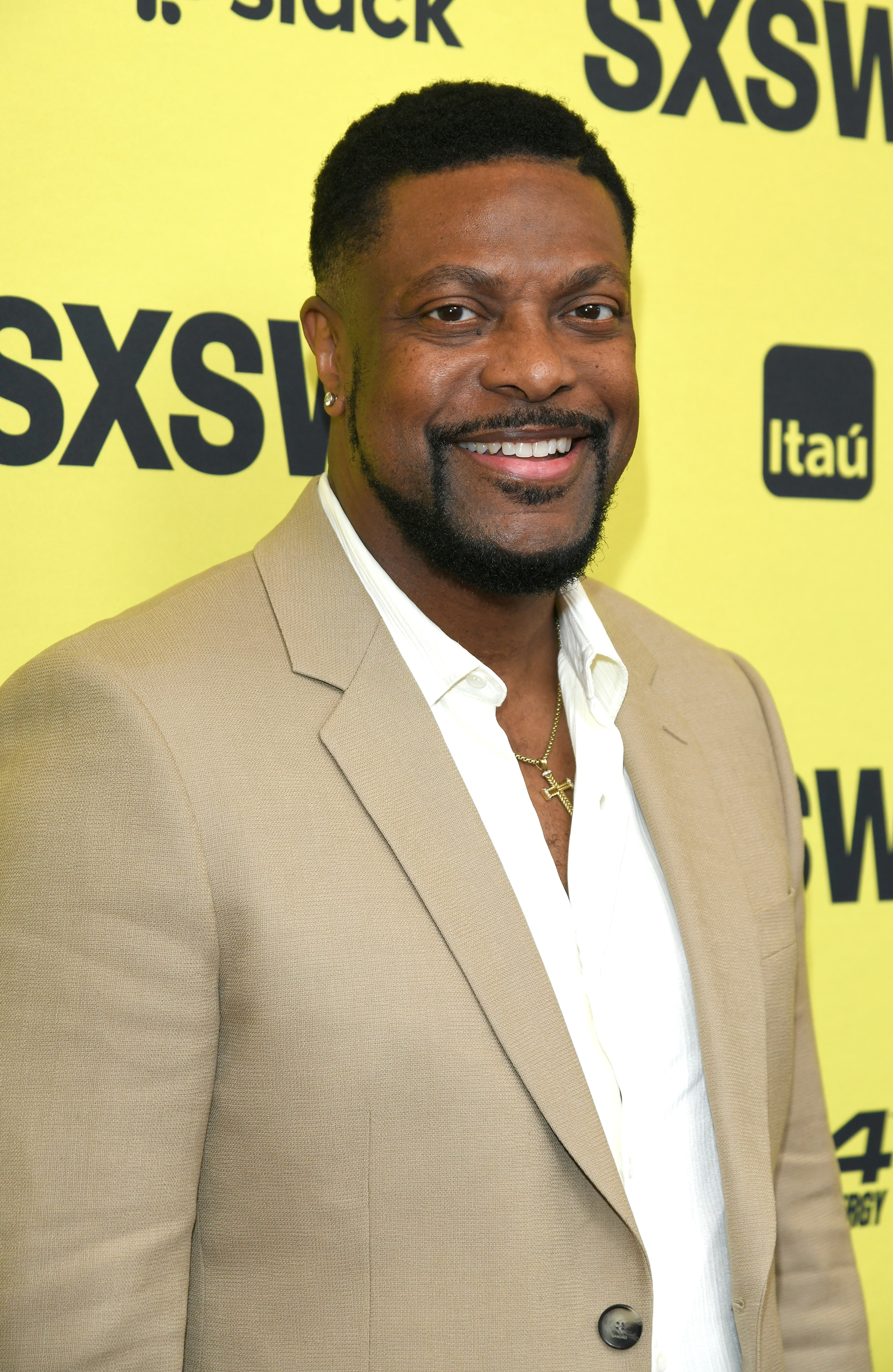 Man in a beige blazer and white shirt smiles at SXSW event backdrop