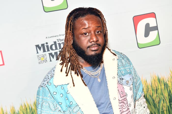 Person on a red carpet wearing layered necklaces and a patterned jacket with a shearling collar