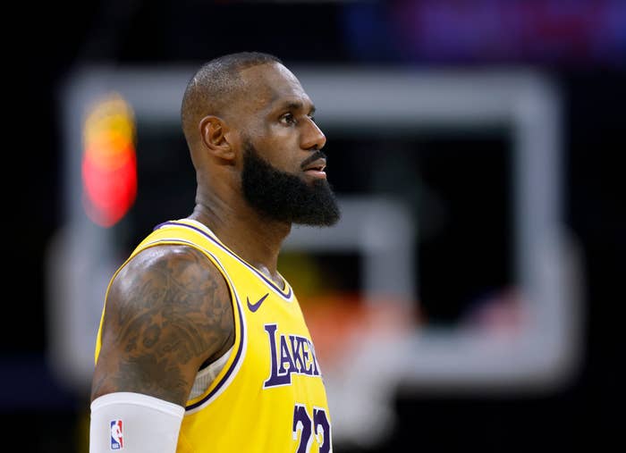 LeBron James in a &quot;Lakers&quot; jersey stands on a court, focused in profile, with a white arm sleeve and tattoos visible on his right arm
