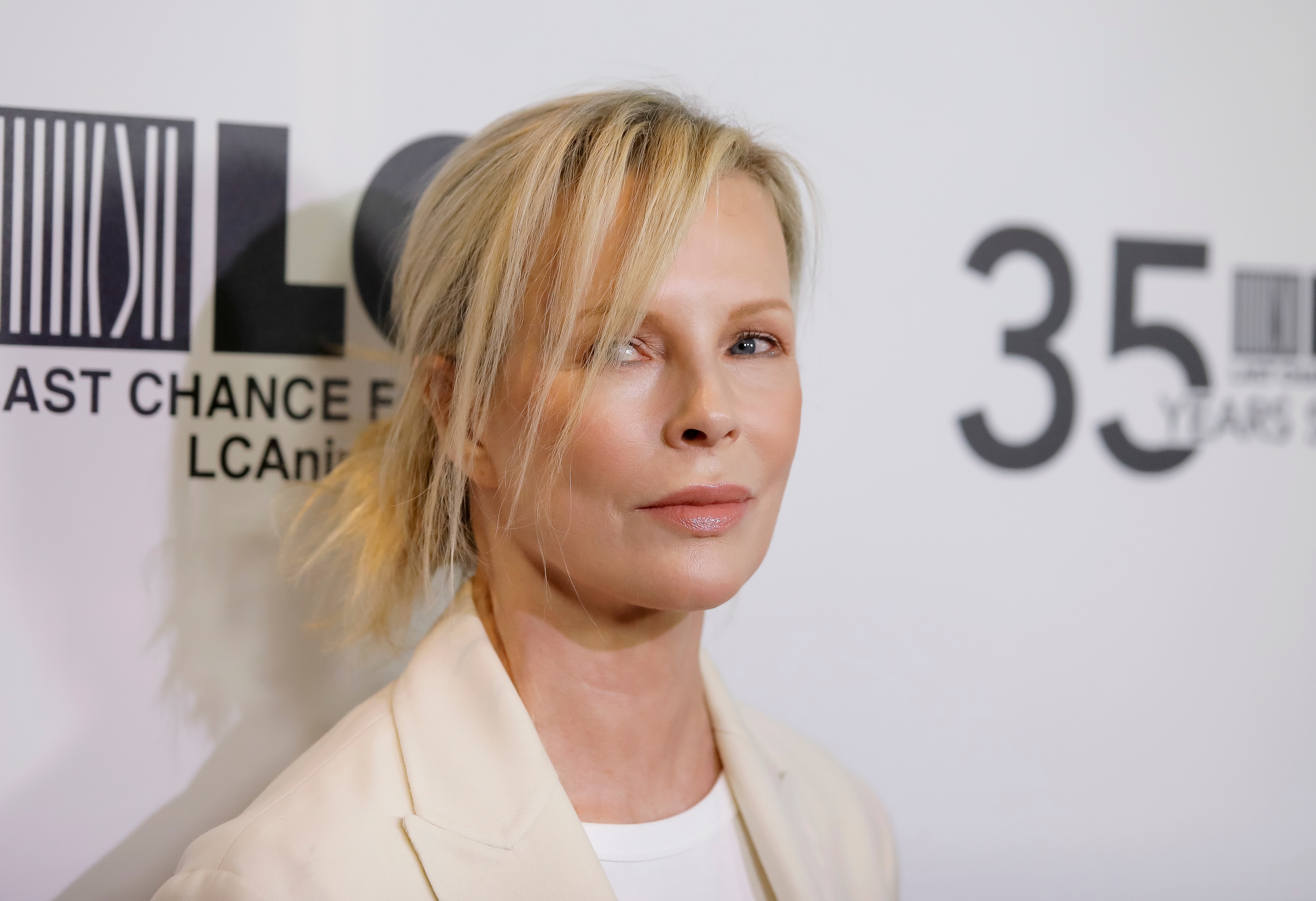 Person in elegant suit poses at a Last Chance for Animals event, standing against a backdrop with the organization&#x27;s logo and event details