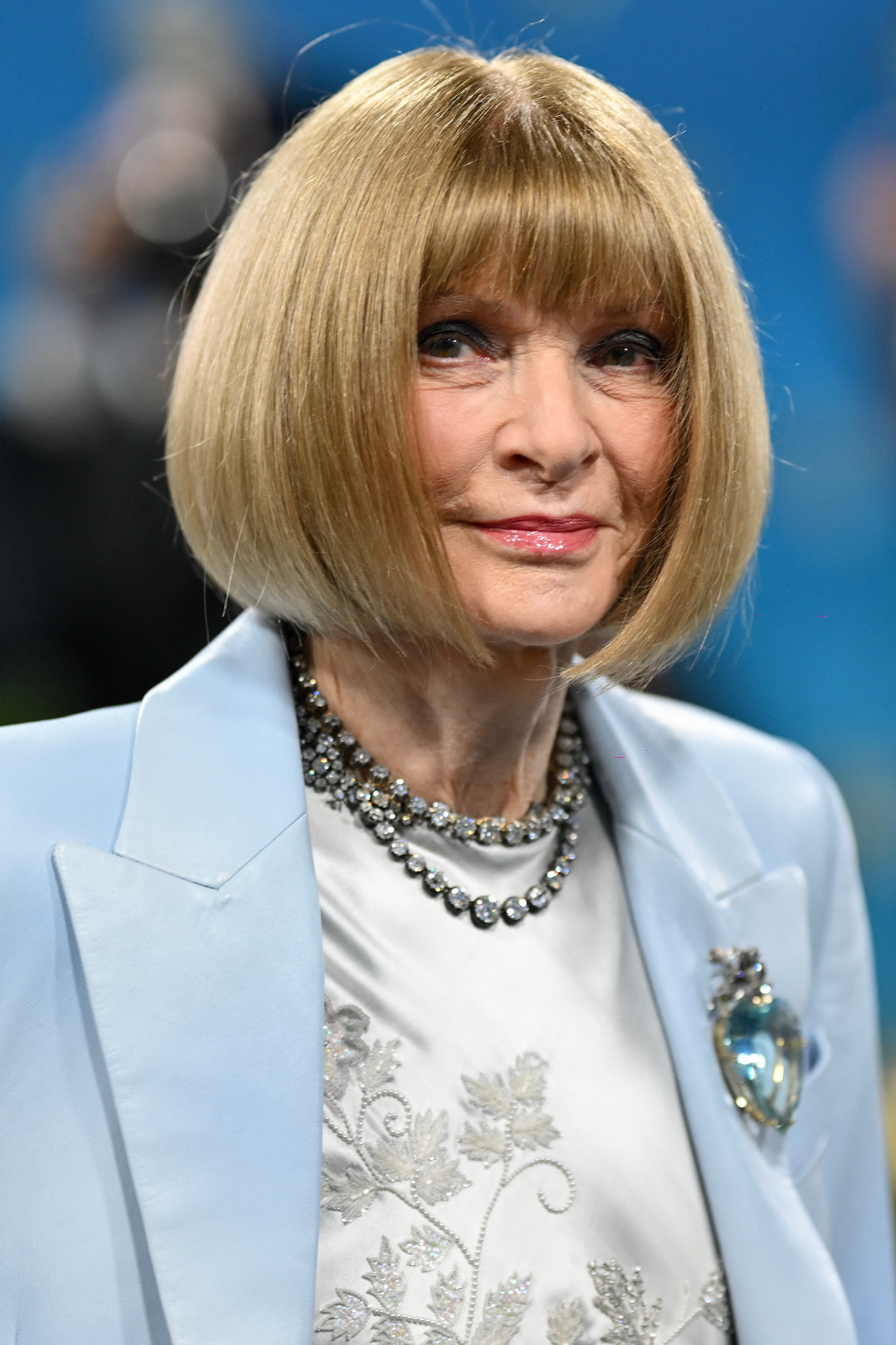 Anna Wintour with short bob hairstyle in elegant attire, featuring a light blazer, silver embroidery, and a statement necklace on a formal occasion