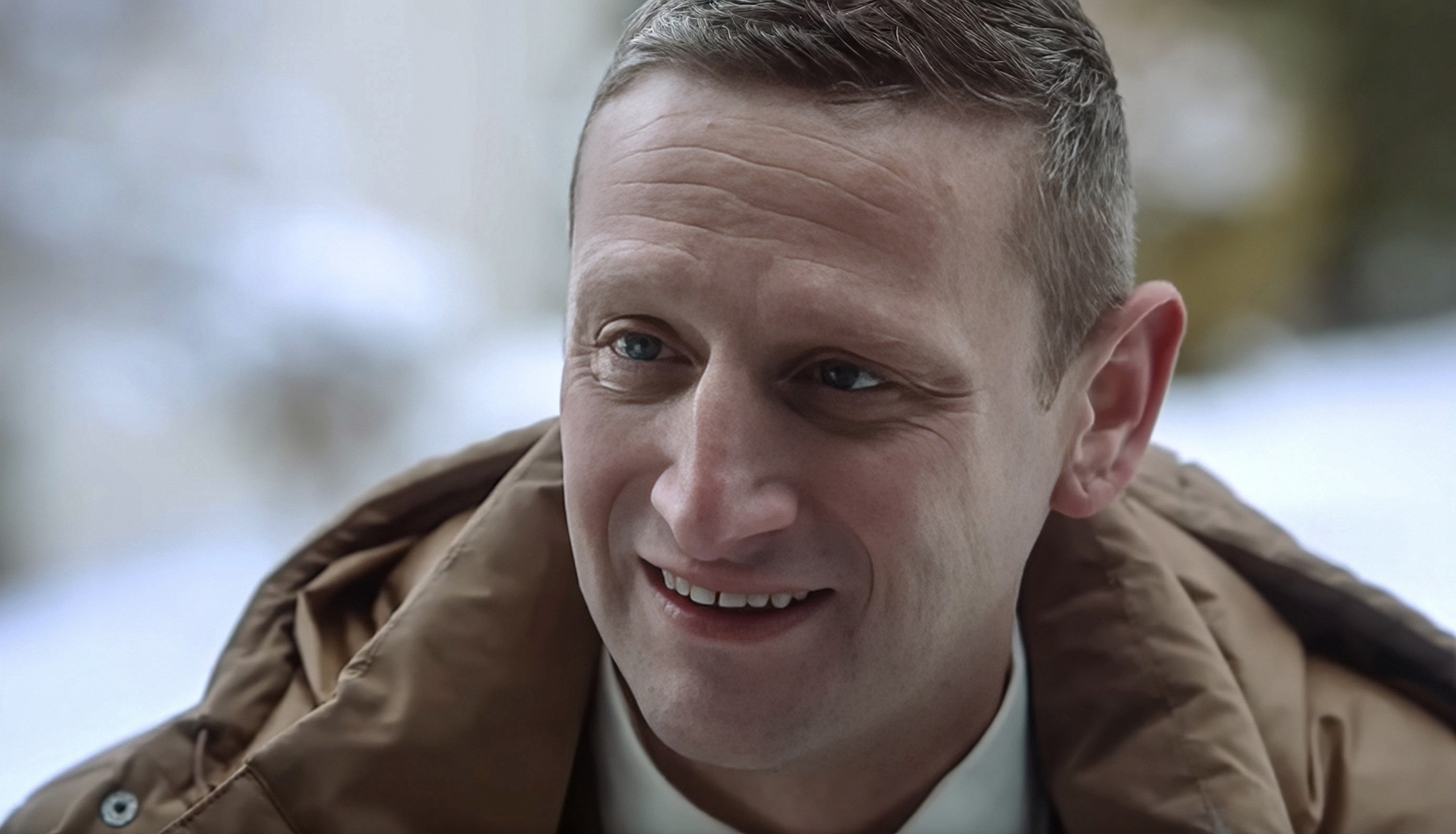 Person outdoors smiling, wearing a coat with the hood down