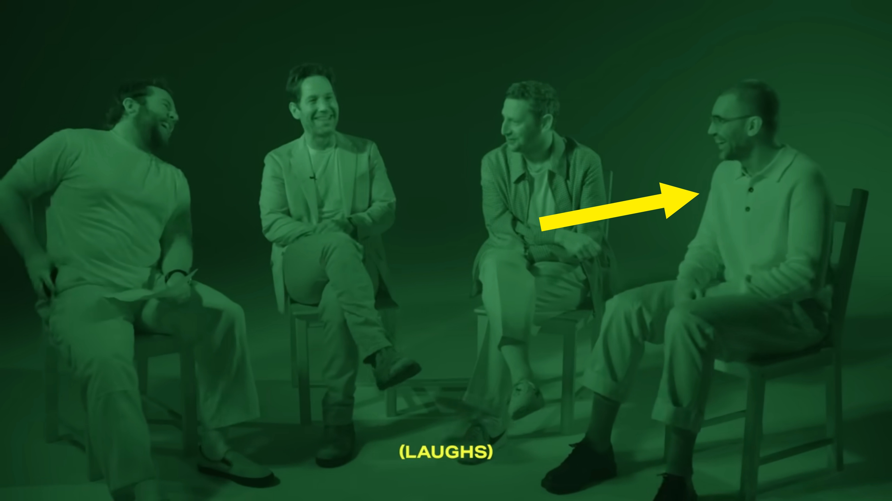 Four people sit in chairs, laughing together in a dimly lit setting