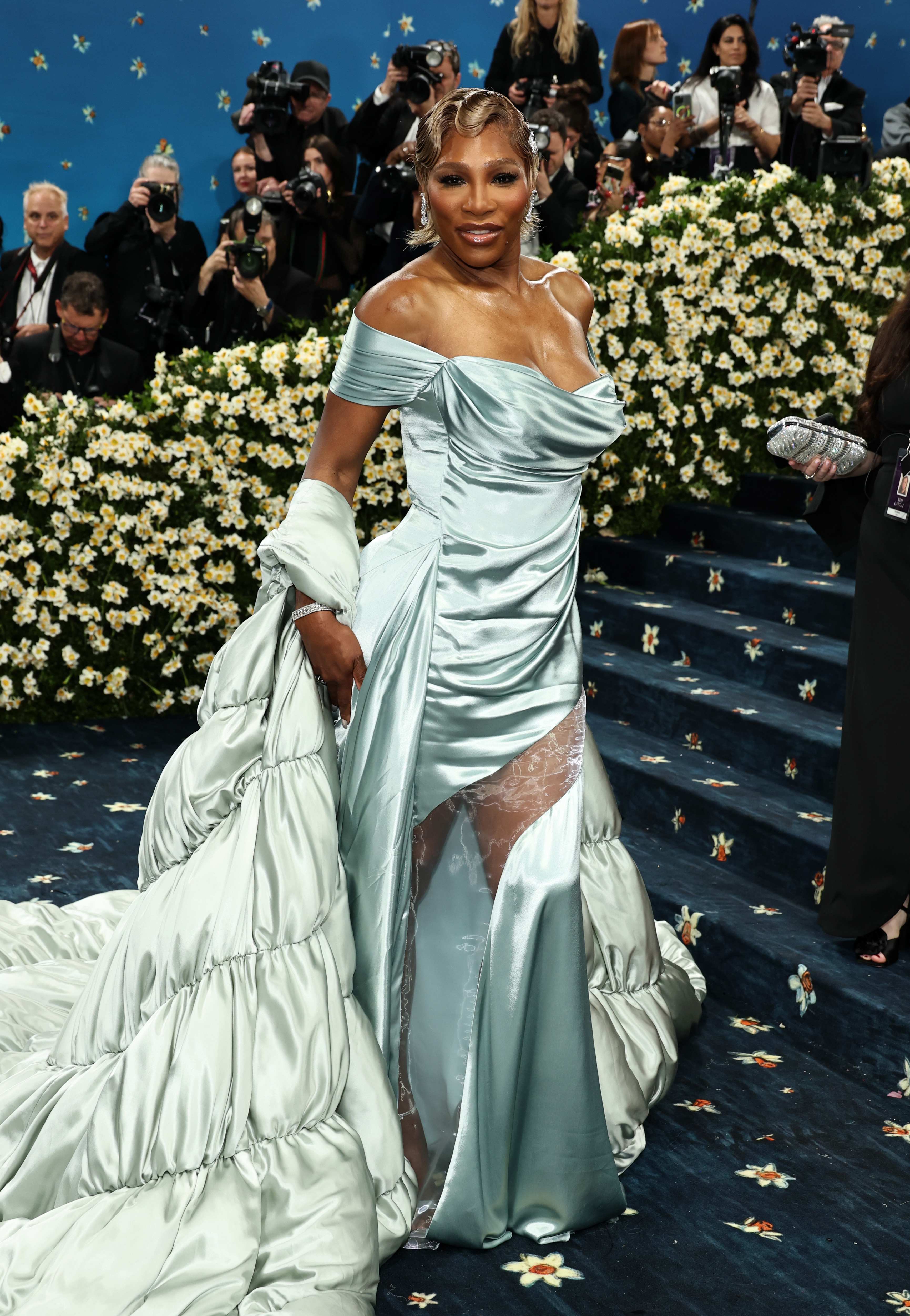 Celebrity in a stylish, satin off-shoulder gown with a long train poses for photographers on a flower-adorned carpet