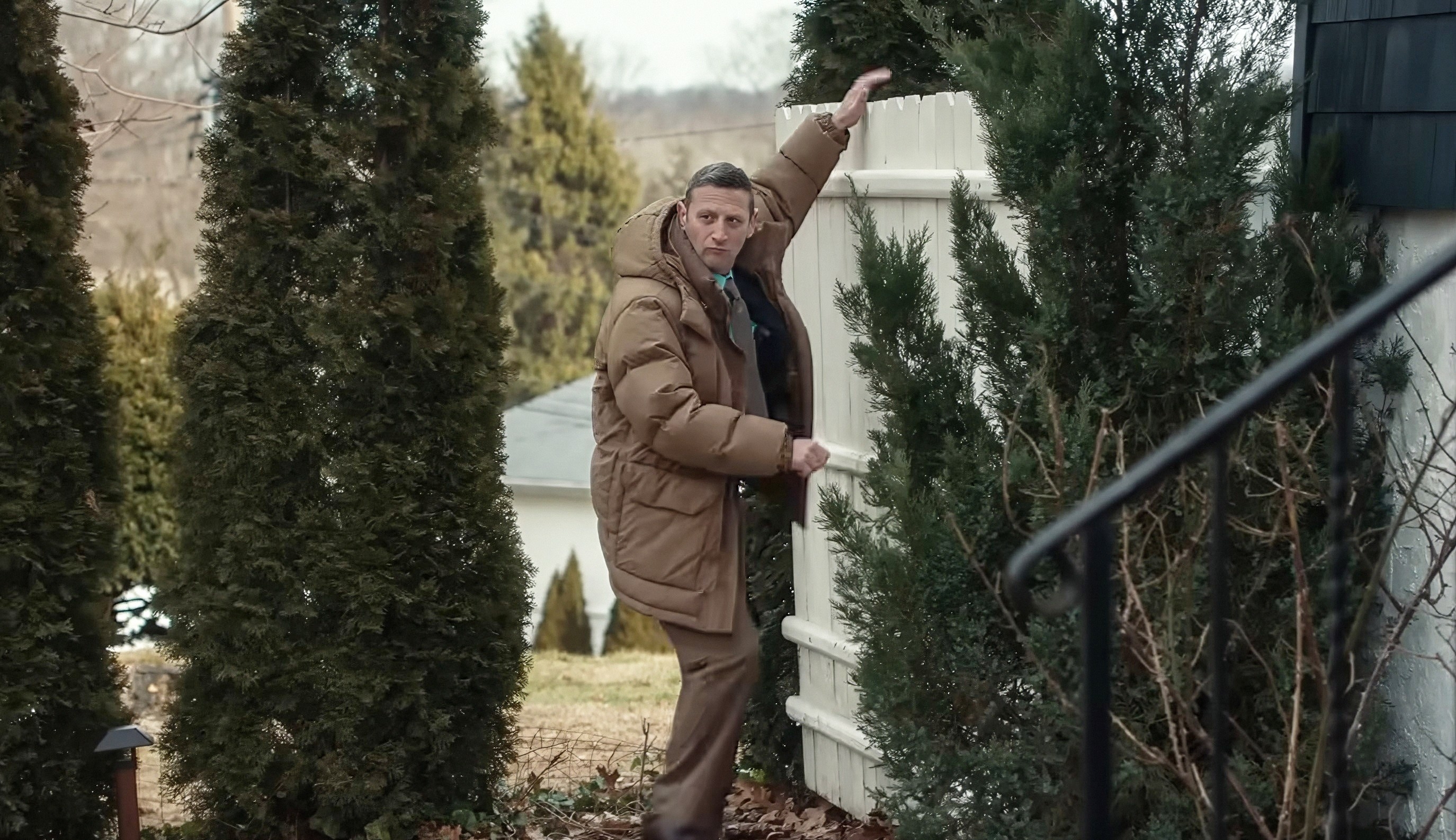 Person in a puffy coat opens a gate, surrounded by tall trees. Cozy, rural setting