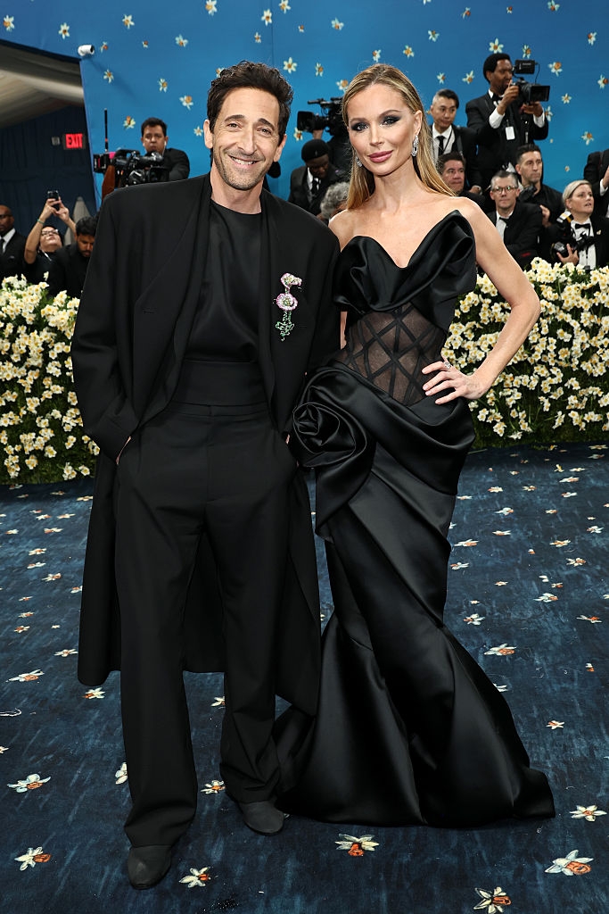 Adrien in a suit with a cloak and floral detail; Georgina gown with sheer panels and floral accents