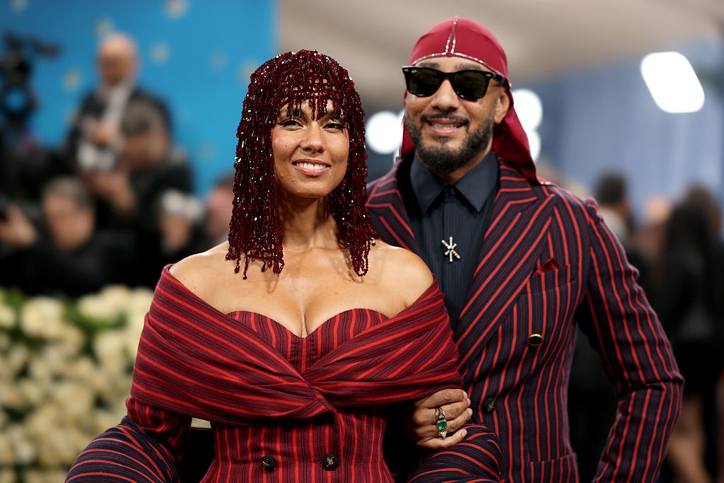 Alicia wears an off-shoulder, striped gown with beaded headpiece. Swizz Beats wears a matching striped suit and headscarf