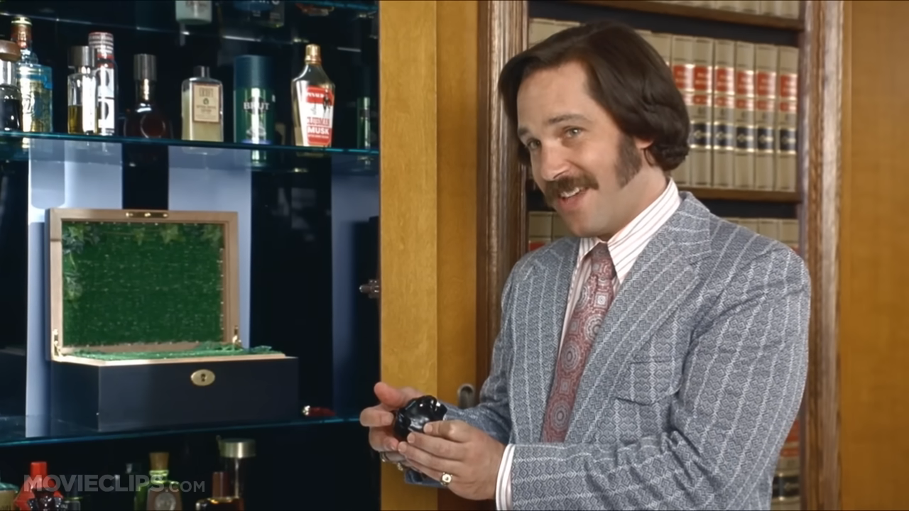 Person in pinstripe suit holding an object, standing by glass cabinet with bottles and books behind