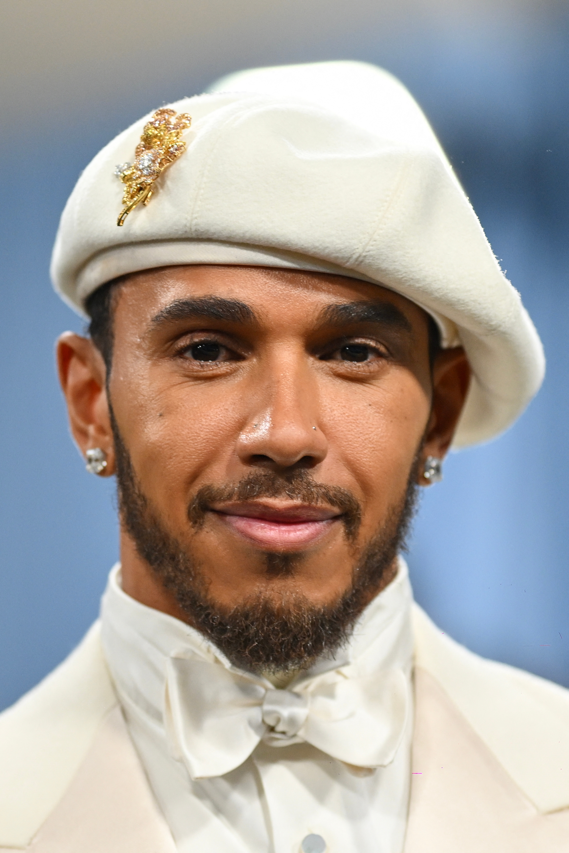 Sir Lewis Hamilton wearing a stylish white beret with embellishment and a matching suit with a bow tie at a formal event